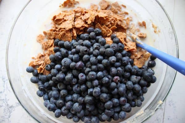 Fresh blueberries and soaked bran flakes being added to the bowl for healthy blueberry bran muffins, just before final mixing.