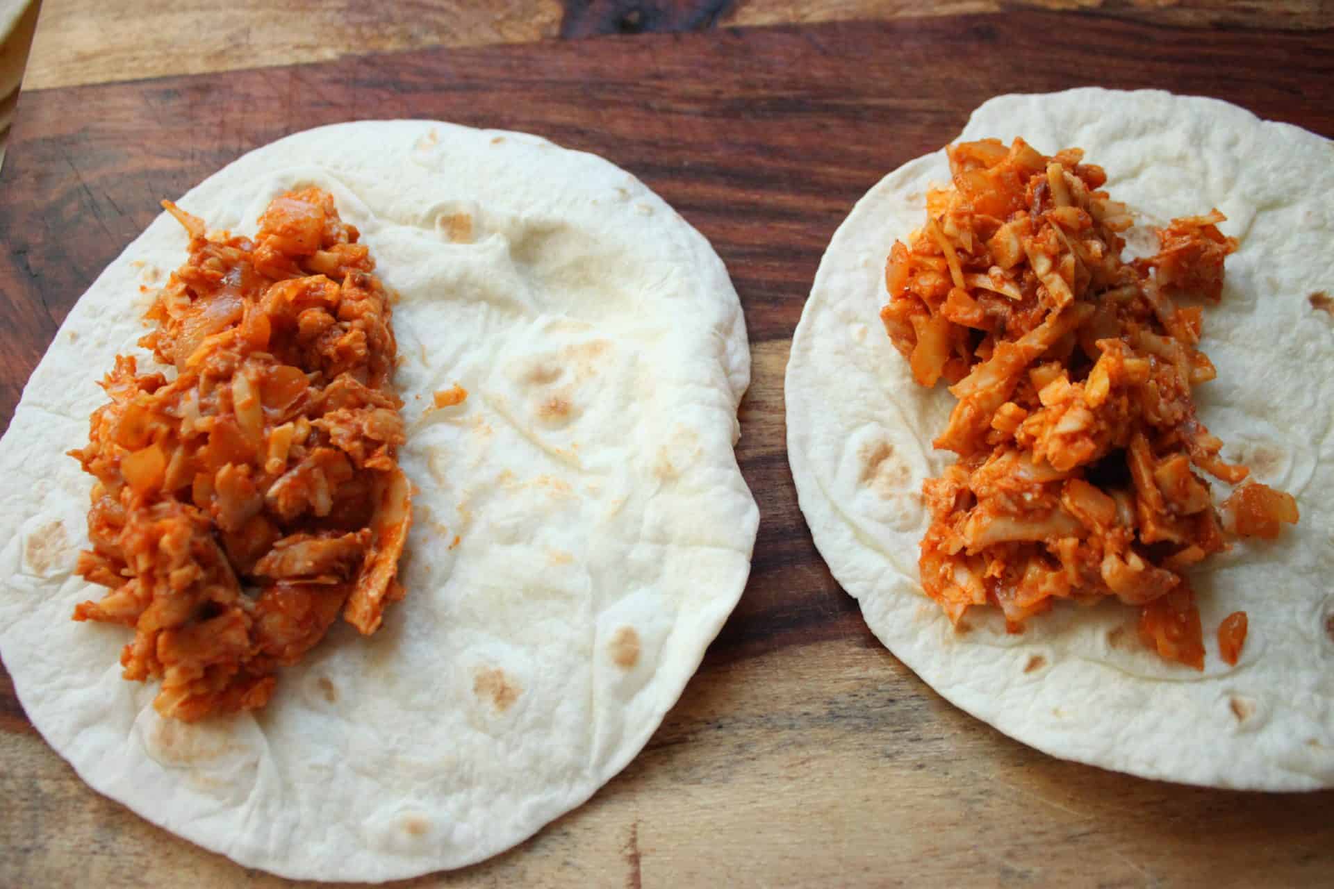 Flour tortillas laid out with spicy chicken filling, ready to be rolled into enchiladas.