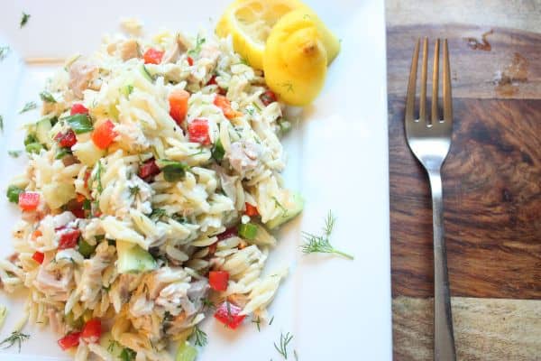Lemon chicken orzo being assembled with visible chopped veggies and chicken, garnished with a lemon wedge and fresh dill.