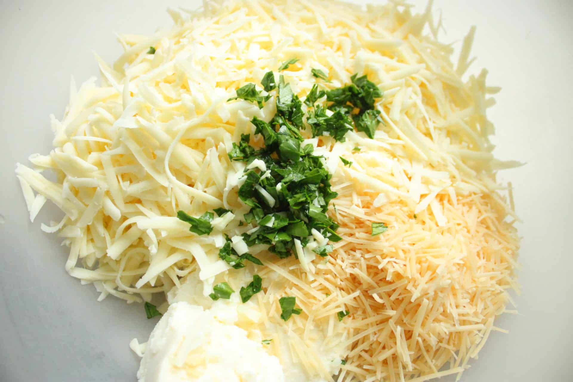 A bowl of shredded cheese, ricotta, and chopped herbs ready to be mixed for the cheese filling in freezer-friendly cheesy baked ziti.