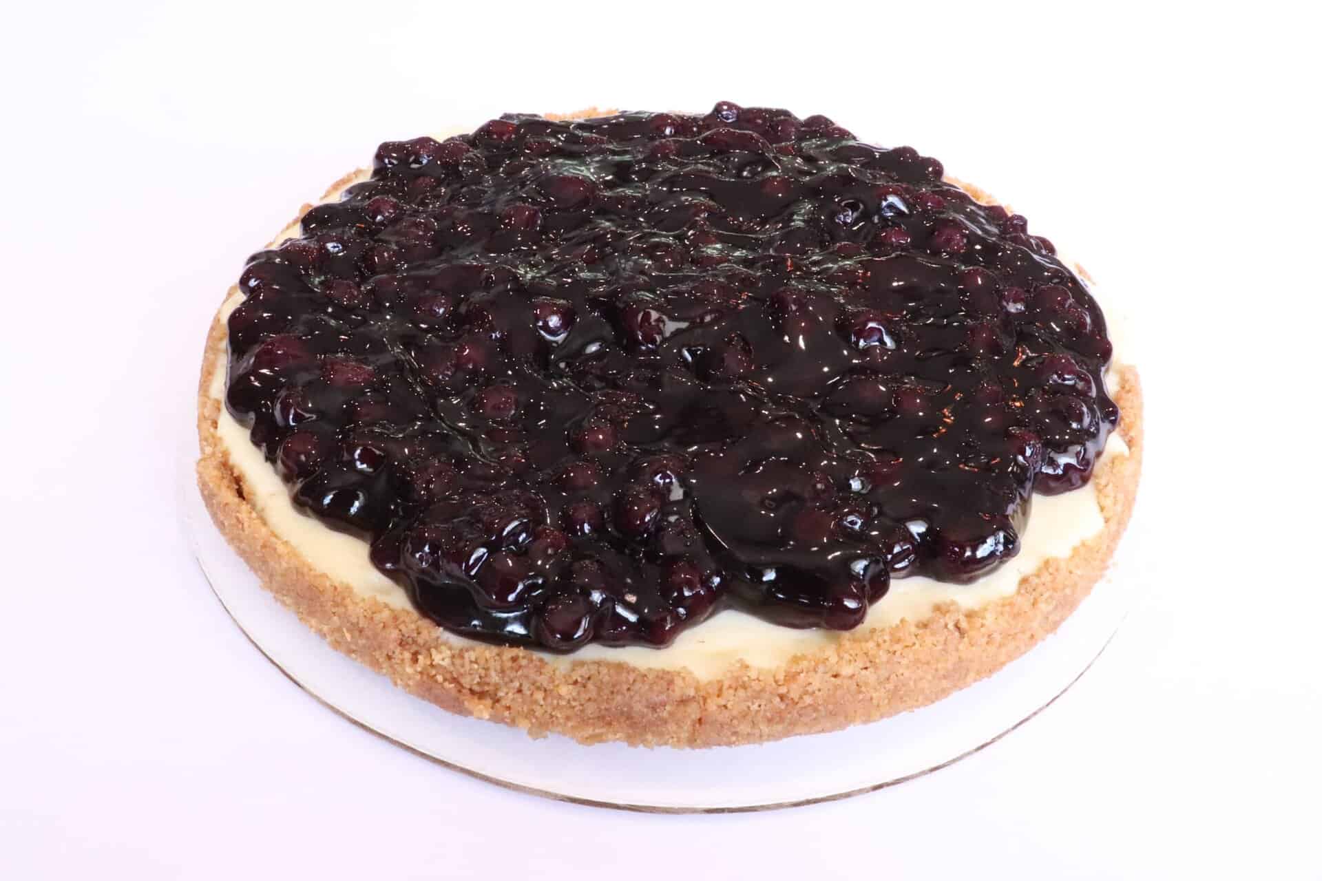Whole blueberry cheesecake topped with a thick layer of glossy blueberries and a golden-brown crust along the edge.