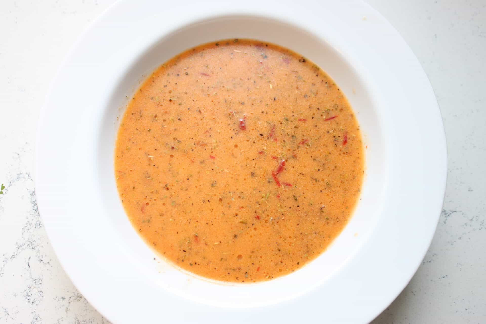 Smooth orange chipotle dressing in a white bowl, made with chipotle peppers, vinegar, lime juice, and honey for black bean and corn salad.