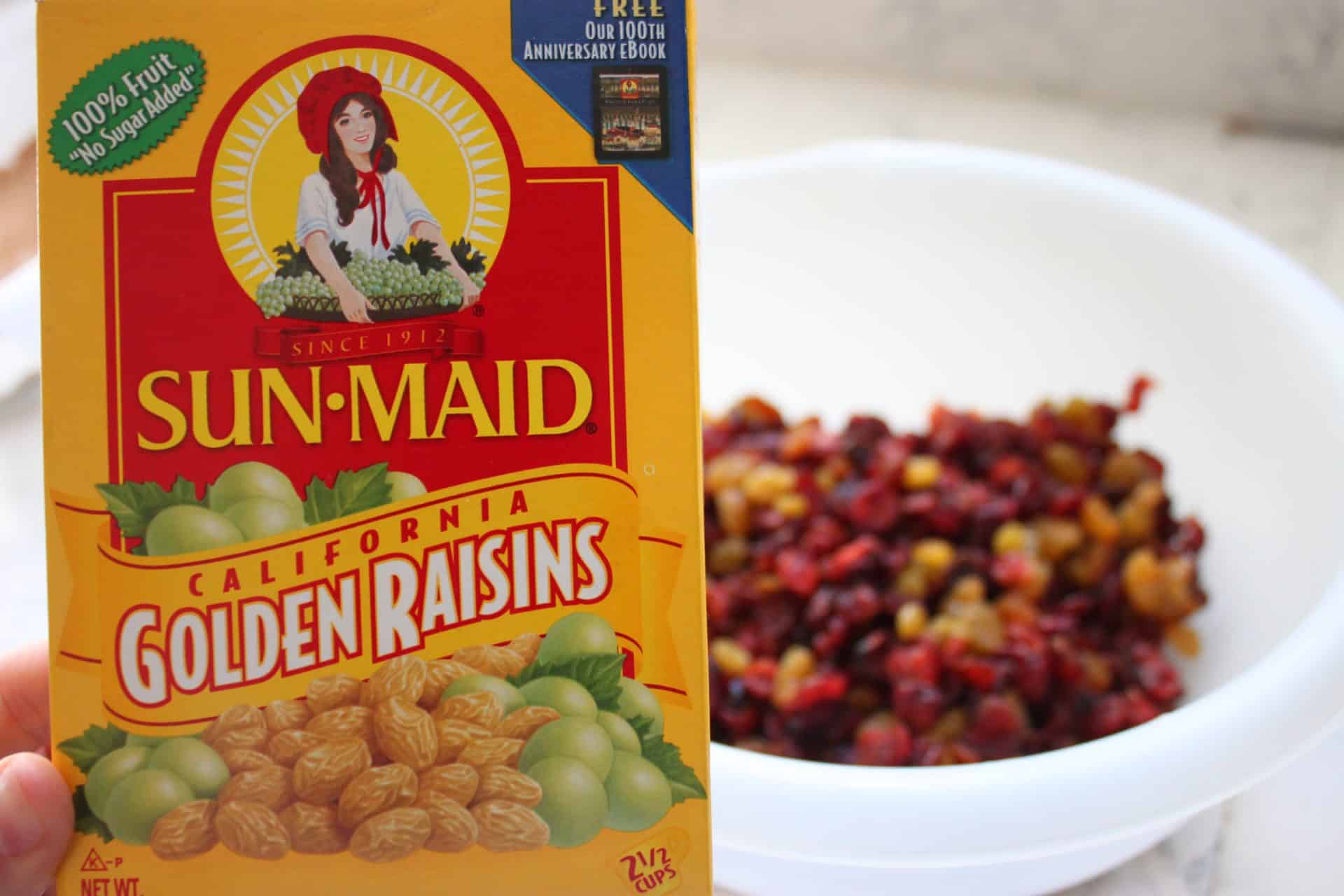 A bowl of golden and red raisins beside a Sun-Maid raisins box, prepped as part of the sweet Coconut Pecan Bars filling mix.