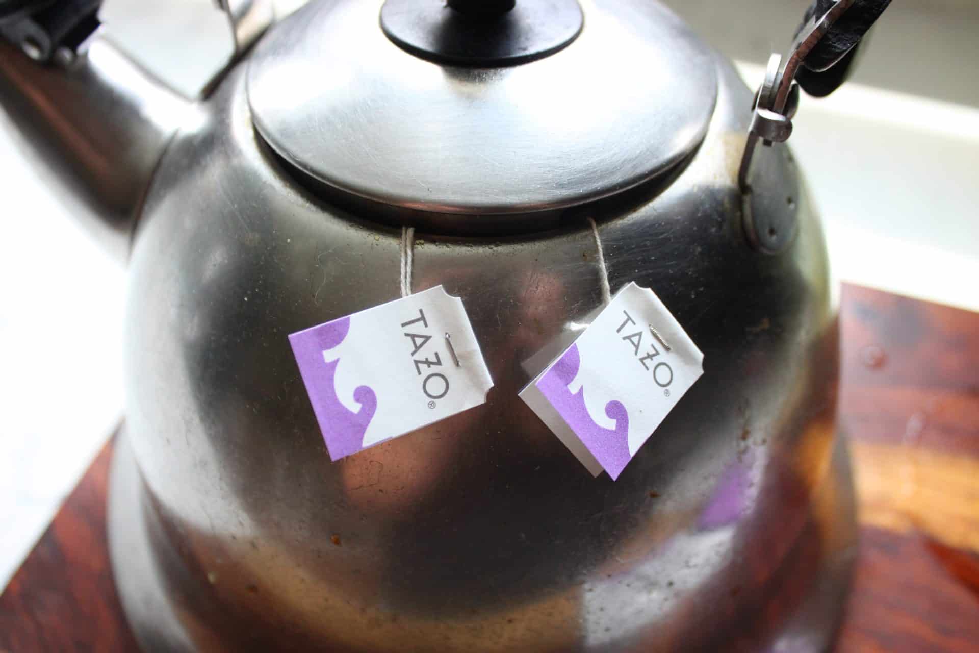 Two Tazo Passion Tea bags hanging from a kettle spout, steeping tea for a Starbucks Iced Passion Tea Lemonade.
