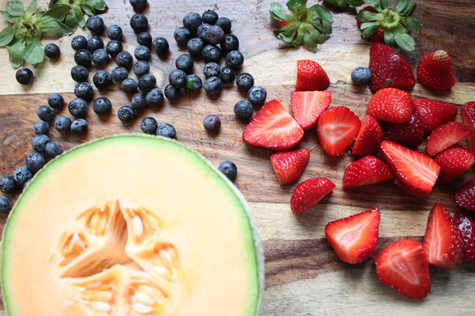Refreshing Cinnamon Coconut Fruit Salad with a Tropical Twist 1 Cantalope, Strawberries, and Blueberries Spread out on a Wood Counter