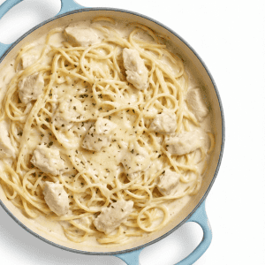 Creamy chicken Alfredo spaghetti in a light blue Dutch oven with herbs