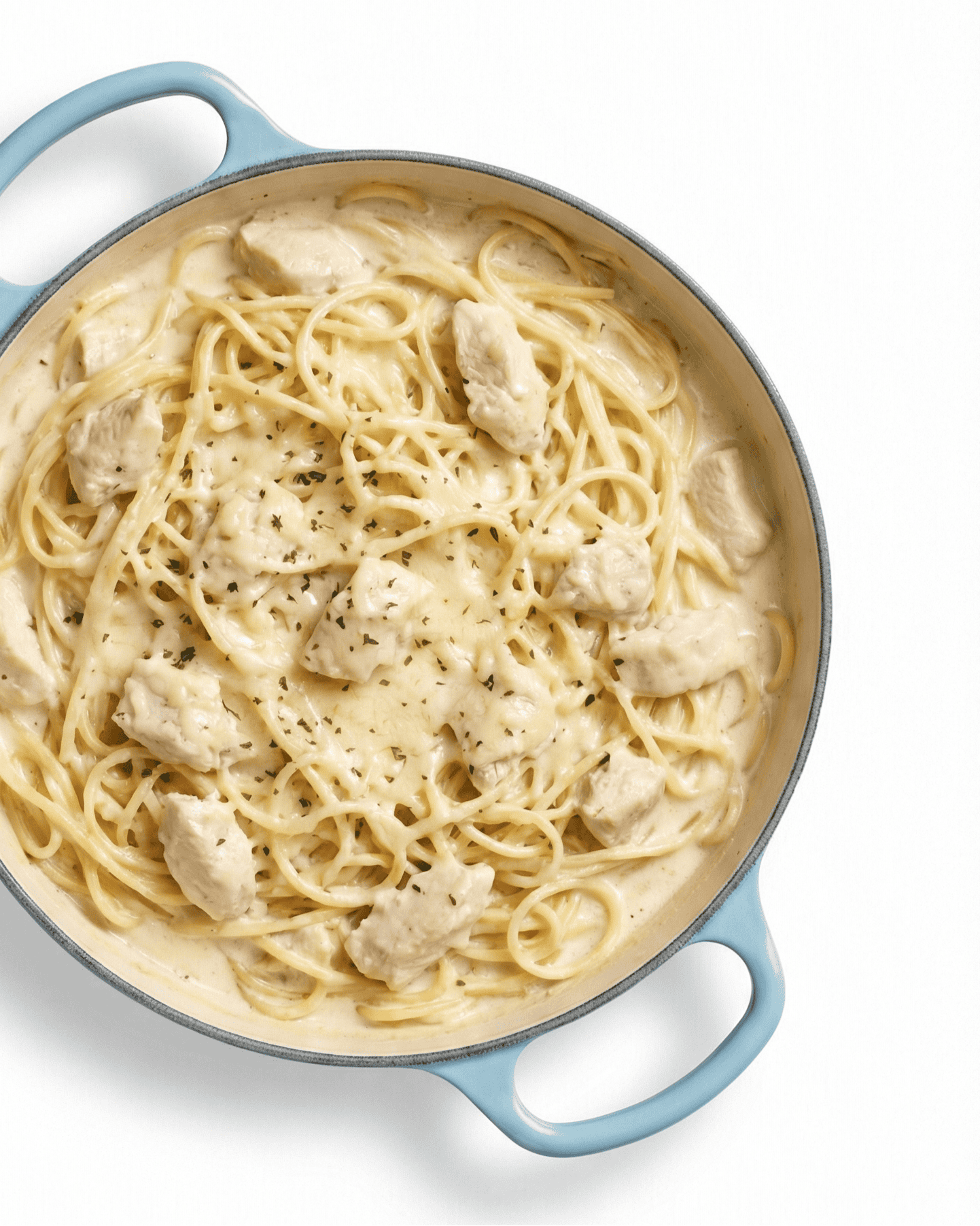 Creamy chicken Alfredo spaghetti in a light blue Dutch oven with herbs