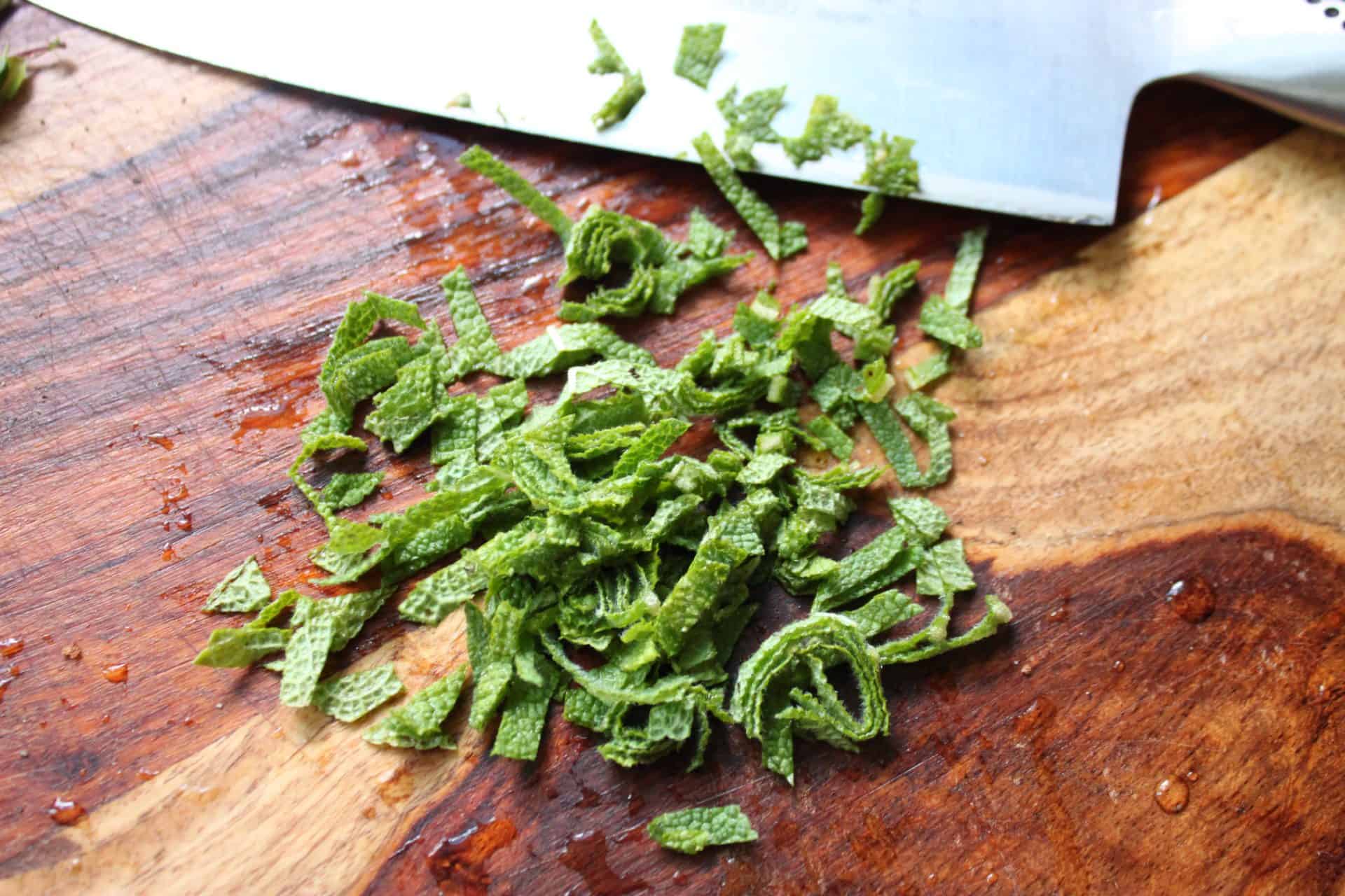 Chiffonade the Sage Leaves with a Butche Knife on a Wood Counter