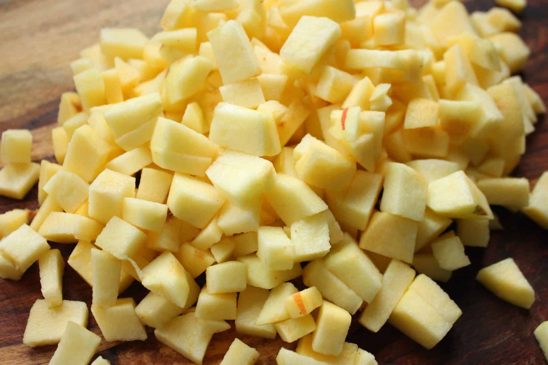 Chopped pieces of fresh yellow apples on a cutting board, ready to be mixed into the cinnamon apple muffins batter.