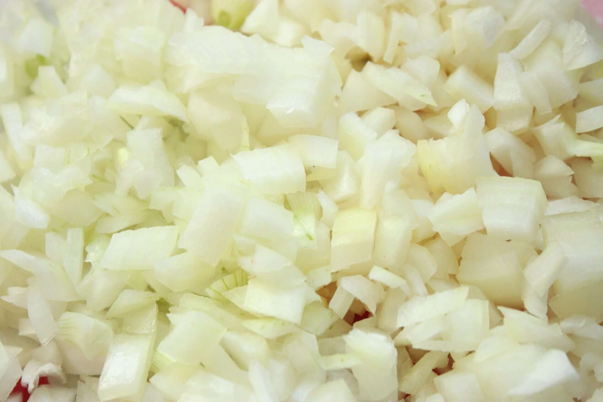 Finely diced onions on a cutting board, ready to be sautéed and added to the filling of spicy chicken enchiladas.