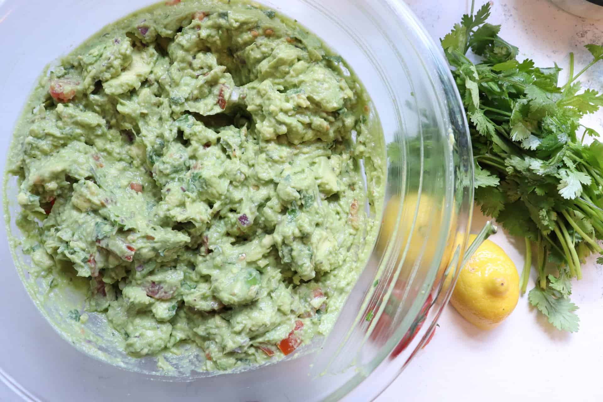 Chunky Restaurant Style Guacamole in a Glass Bowl with Lemon Tomatoe and Herbs on the Side