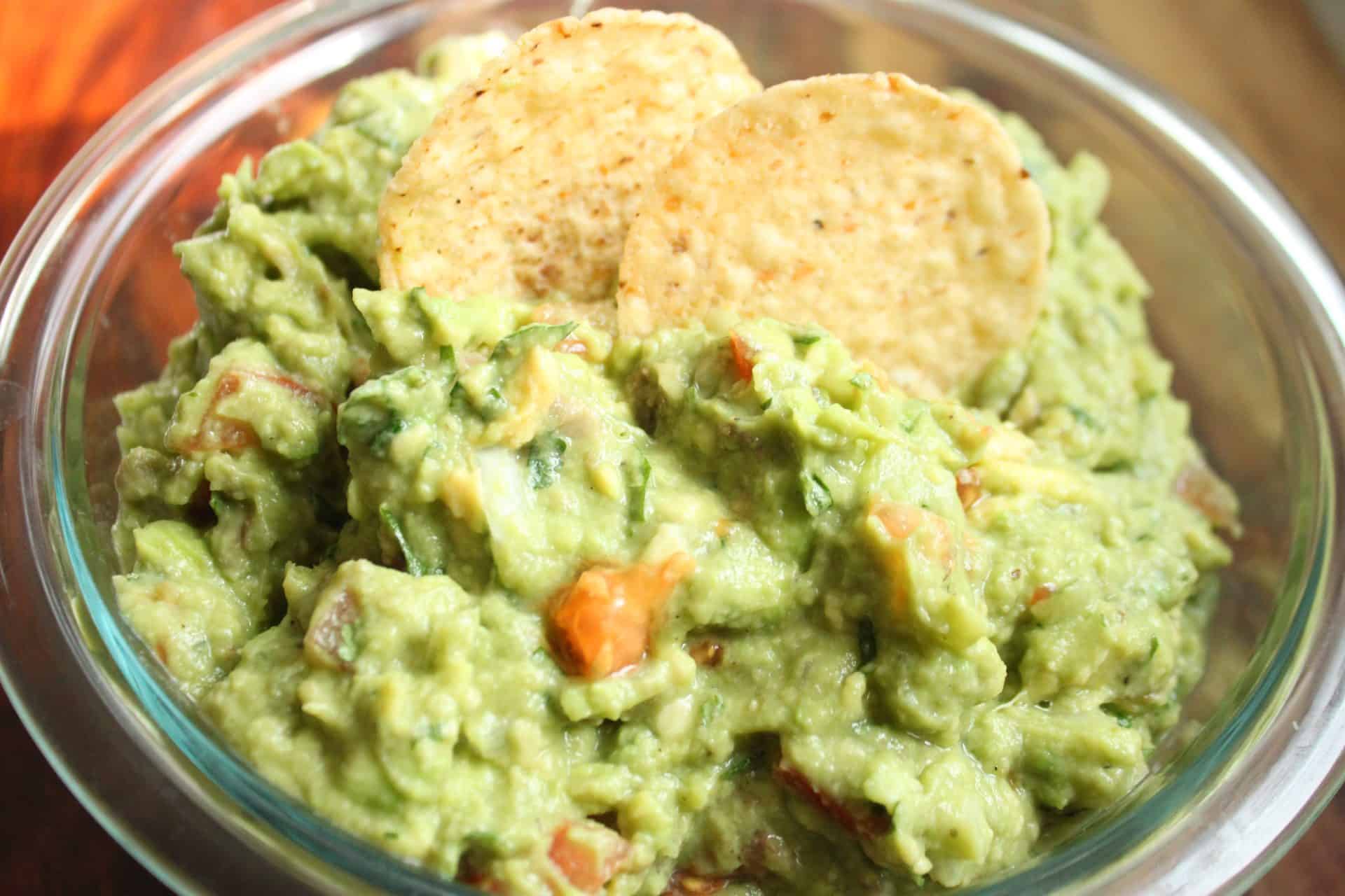 How to Make Flavor-Packed Green Chile Chicken Enchiladas at Home 13 A bowl of chunky guacamole with fresh avocado, tomatoes, and cilantro, served with crispy tortilla chips as a side.