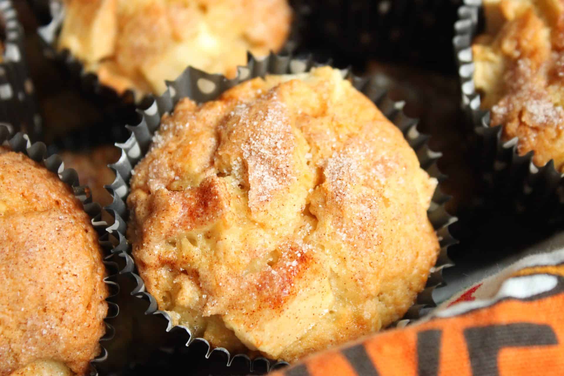 Close-up of a single cinnamon apple muffin with a golden crust, showcasing the sugary top and visible apple pieces inside.