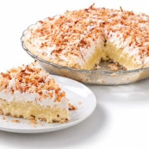 Slice of coconut cream pie showing creamy filling and soft topping, with the whole pie behind it missing one slice.