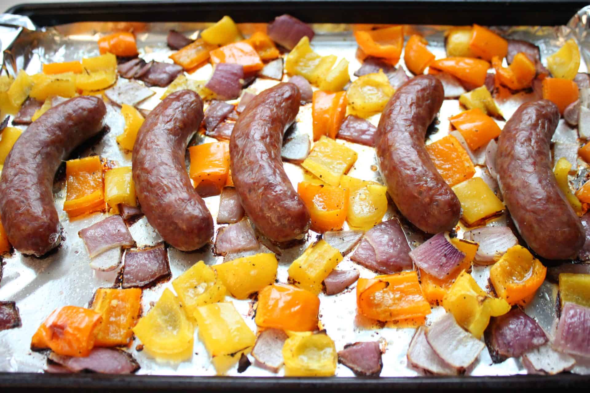 Sheet pan with cooked Italian sausages, golden bell peppers, and caramelized onions just out of the oven for hoagie sandwiches.