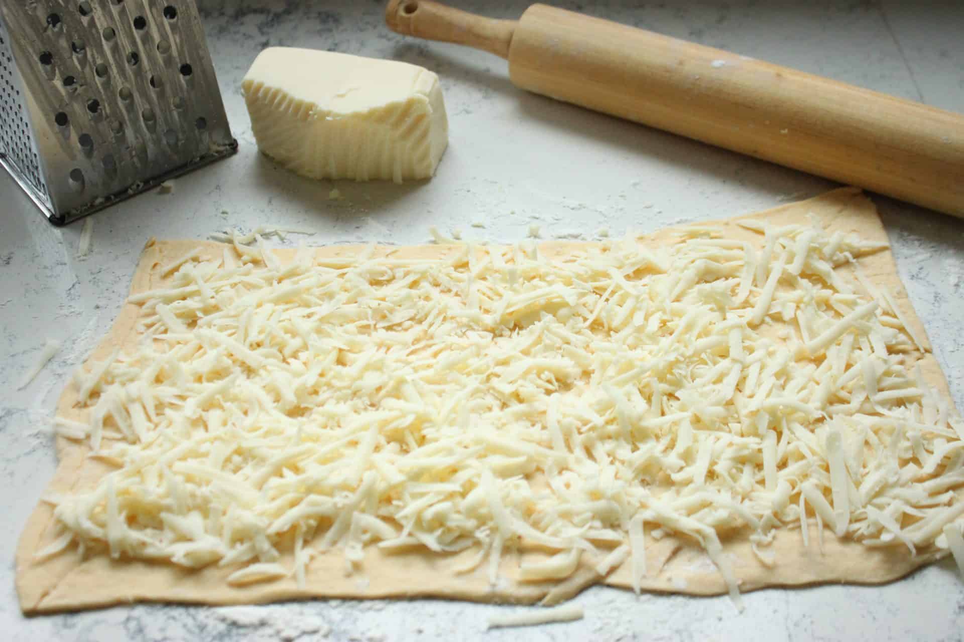Savory and Sweet Ham and Pineapple Pinwheels for the Family 1 A baking sheet with crescent roll dough topped generously with shredded mozzarella cheese, ready for ham and pineapple pinwheels.