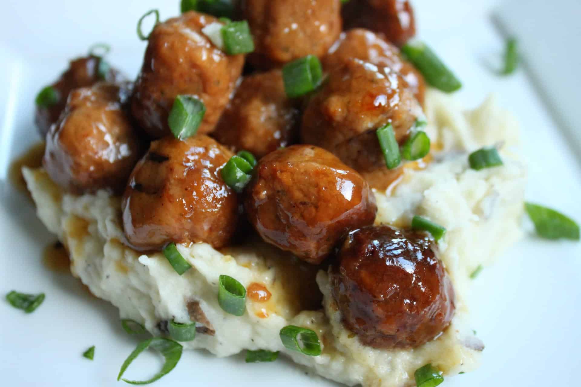 Crockpot Sweet and Sour Meatballs on Top of Mashed Potatoes and Garnished with Green Onions