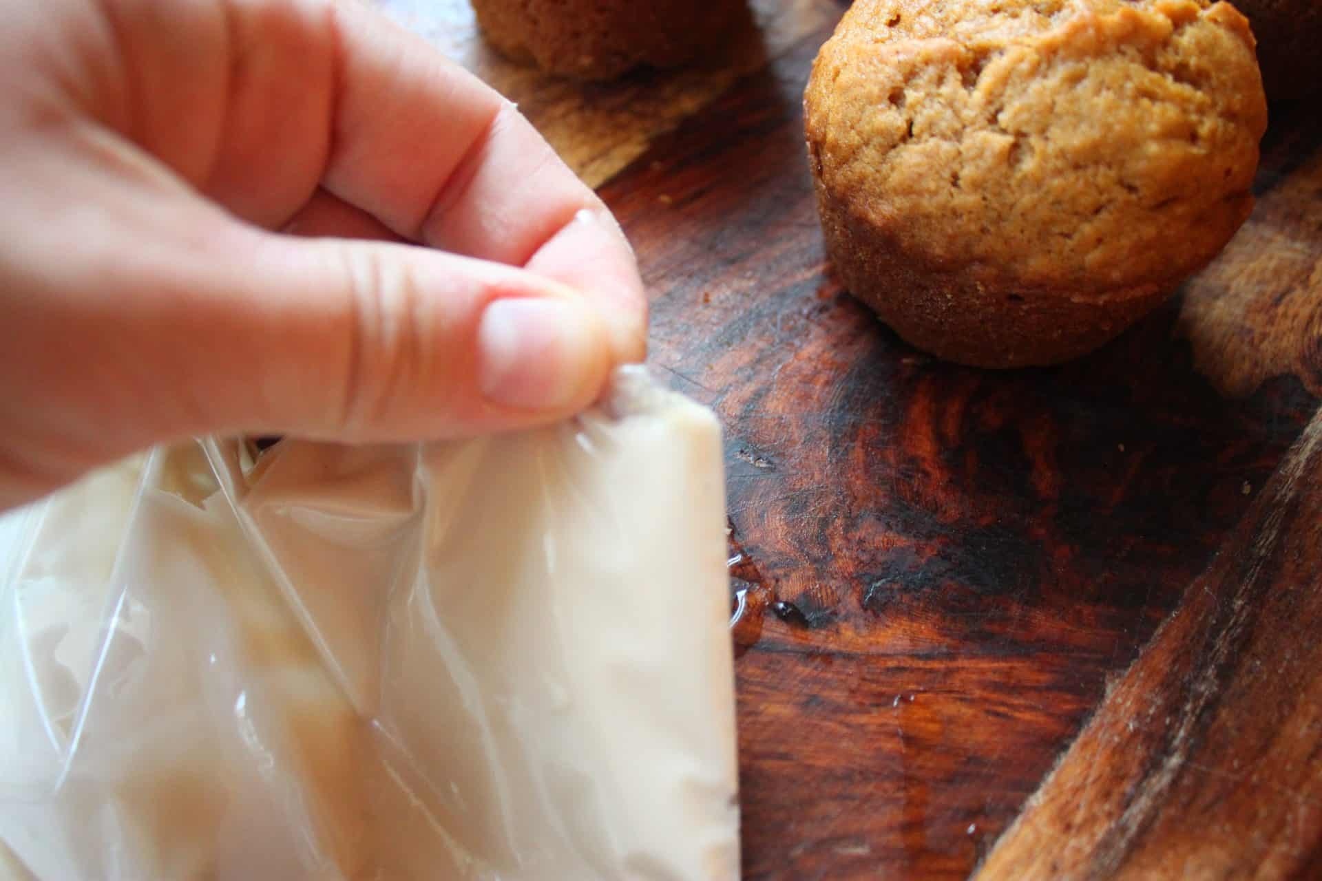 Corner of Zip Lock Bag Cut Off to Drizzle Vanilla Frsoting on Pumpkin Muffins