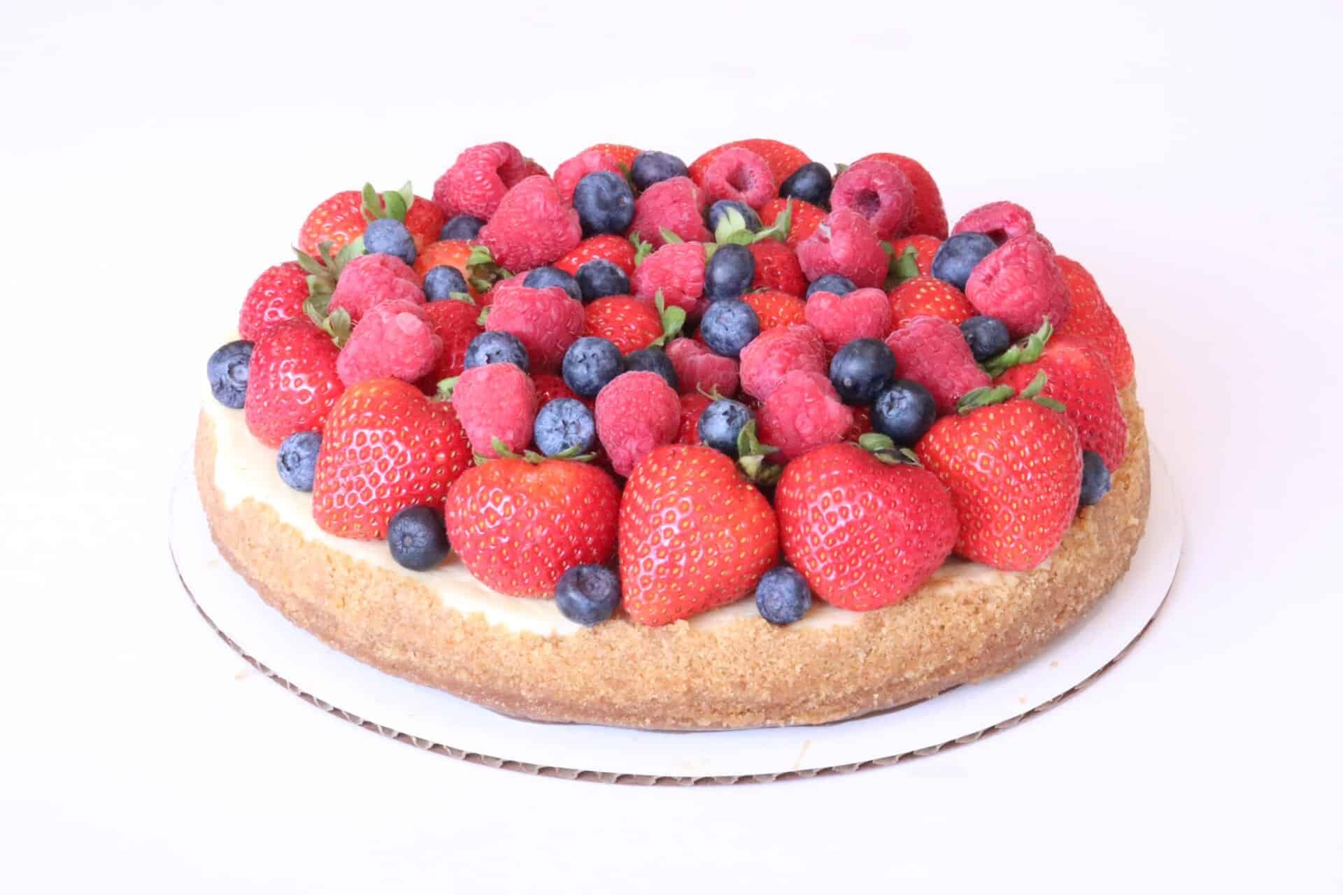 Whole fresh fruit cheesecake topped with a generous assortment of strawberries, blueberries, and raspberries.