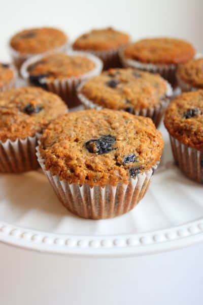Baked healthy blueberry bran muffins cooling in liners, showing golden tops and bits of berry throughout each fluffy muffin.
