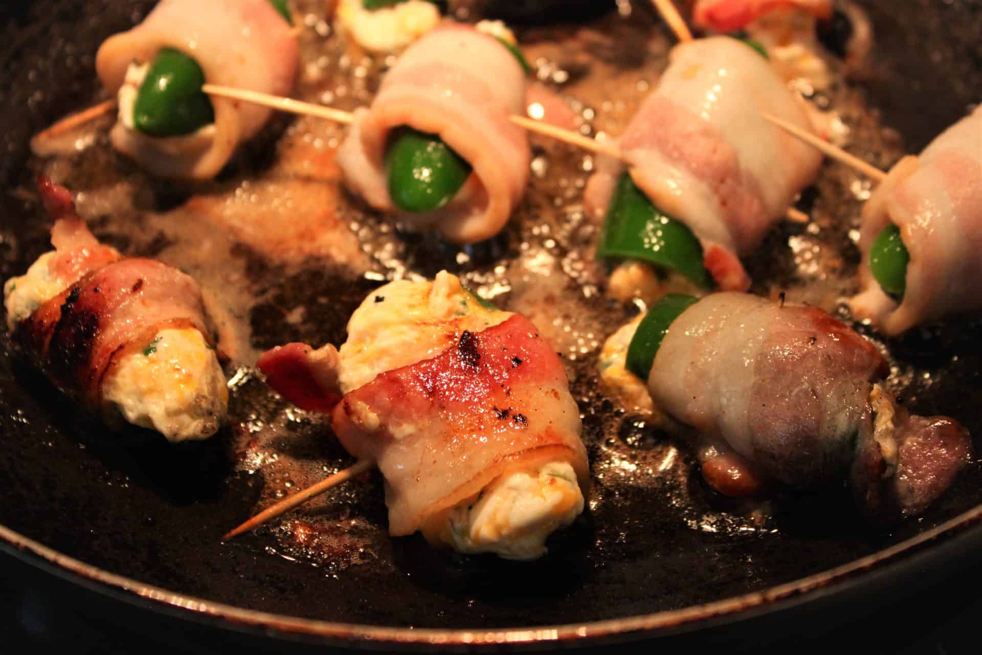 Crispy and Creamy Easy Bacon Wrapped Jalapeño Poppers Recipe 7 Bacon wrapped jalapeño poppers sizzling in a hot pan, showing crispy bacon and melted cheese filling.