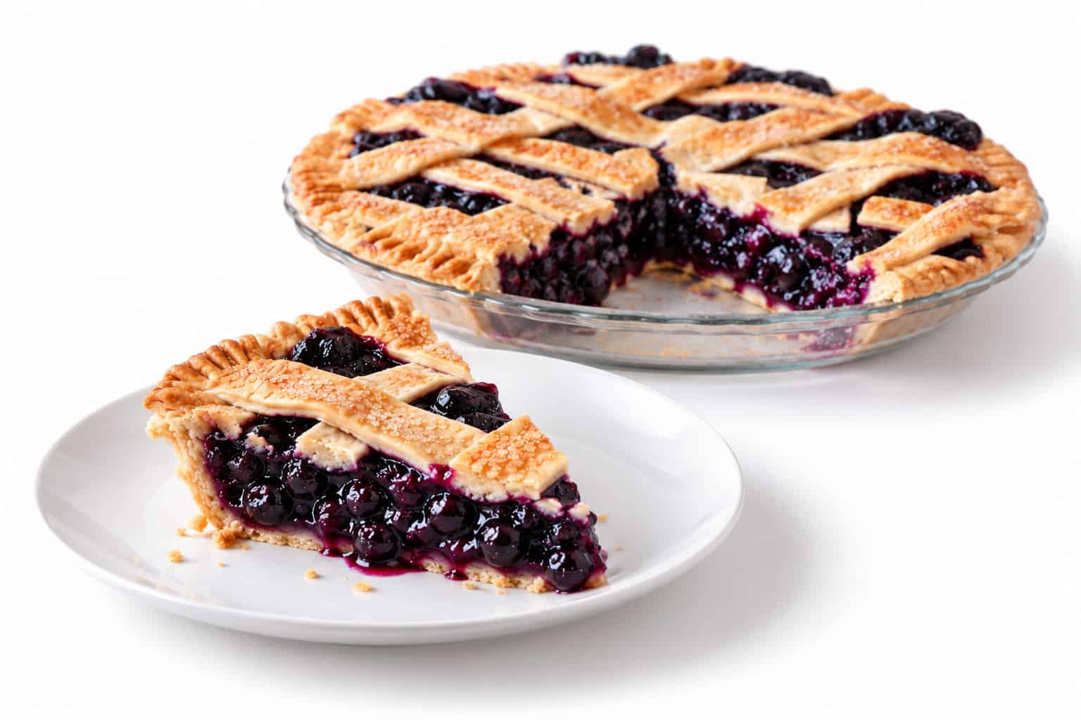 Slice of blueberry pie on a white plate with juicy berry filling and the remaining lattice pie behind it.