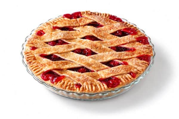 Cherry lattice pie in a shallow clear glass dish, photographed at a 45-degree angle on a bright white studio background.