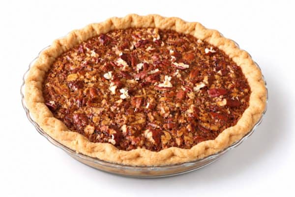 Whole pecan pie at a three-quarter angle, showing the golden crust, pecan-covered top, and clear glass dish.