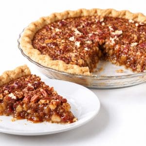 Pecan pie slice on a plate with glossy filling, with the whole pie missing one slice behind it. Title: Pecan Pie Slice Served