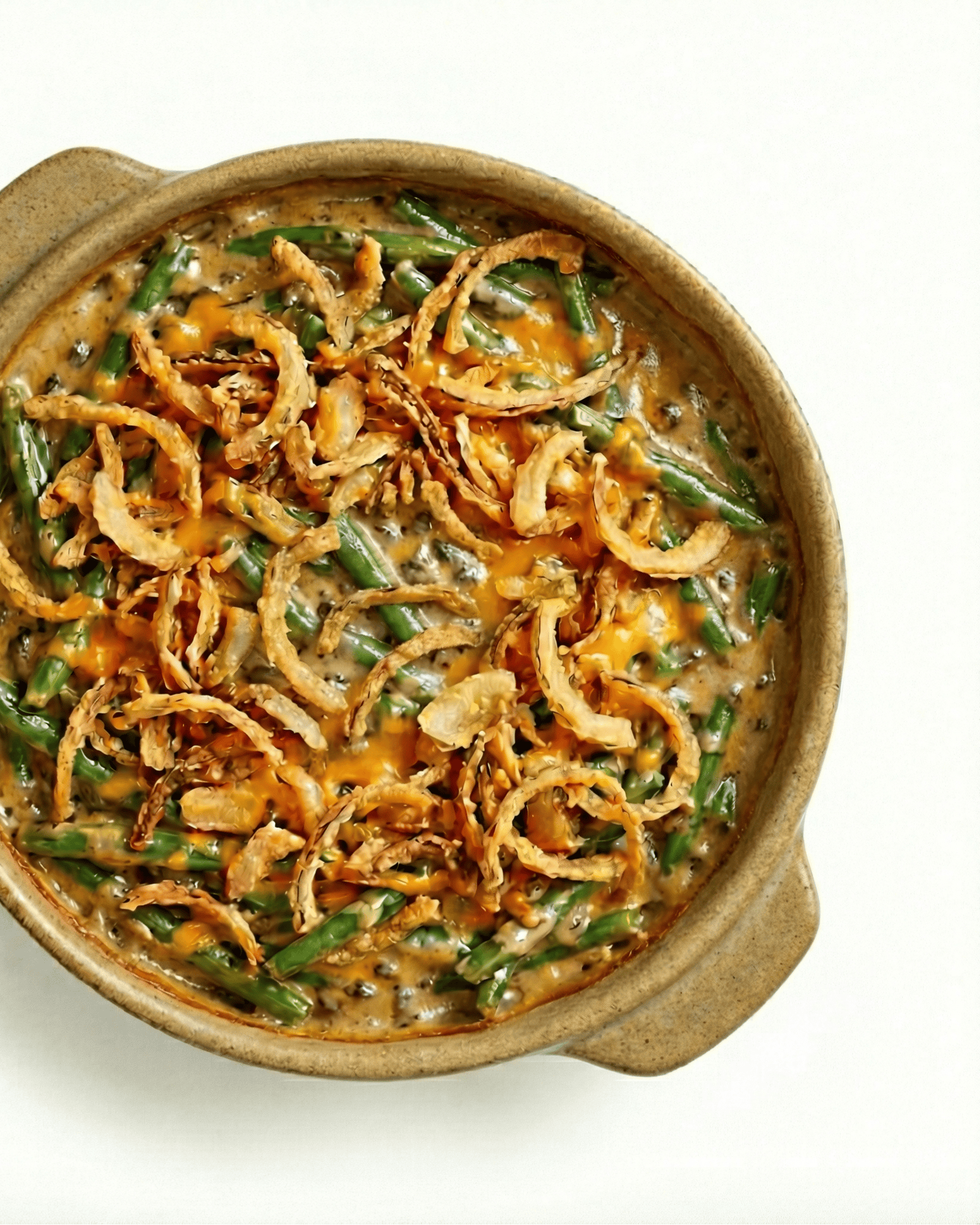 Green Bean Casserole 1 Green bean casserole with creamy mushroom sauce, melted cheese, and crispy fried onions in tan ceramic dish