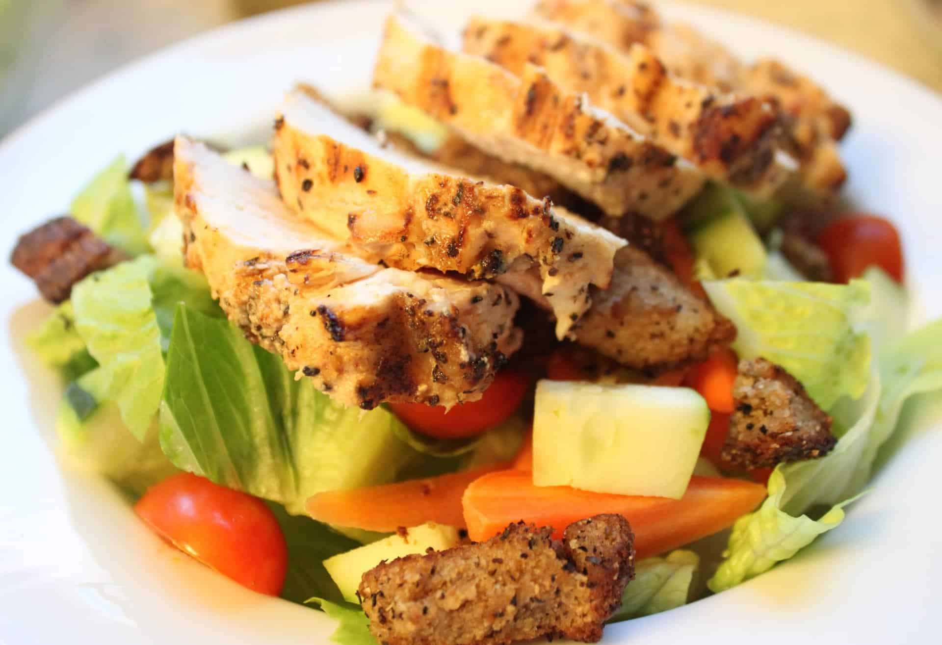 Upclose Picture of Grilled Chicken Slices Placed on Top of Caesar Salad with Carrots, Tomatoes, Salad, and Croutons