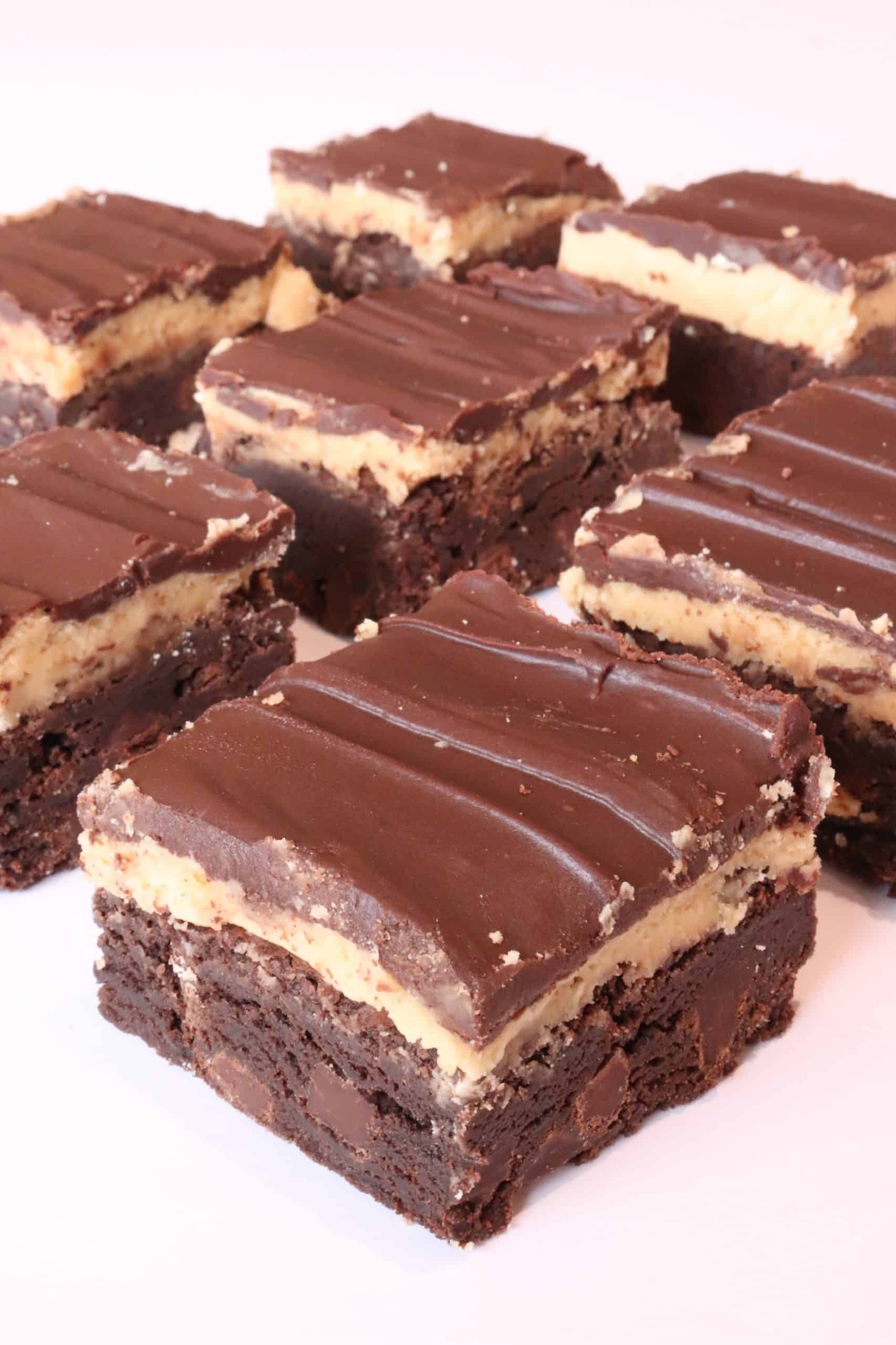 Several rich chocolate brownies topped with a creamy peanut butter layer and a smooth chocolate ganache