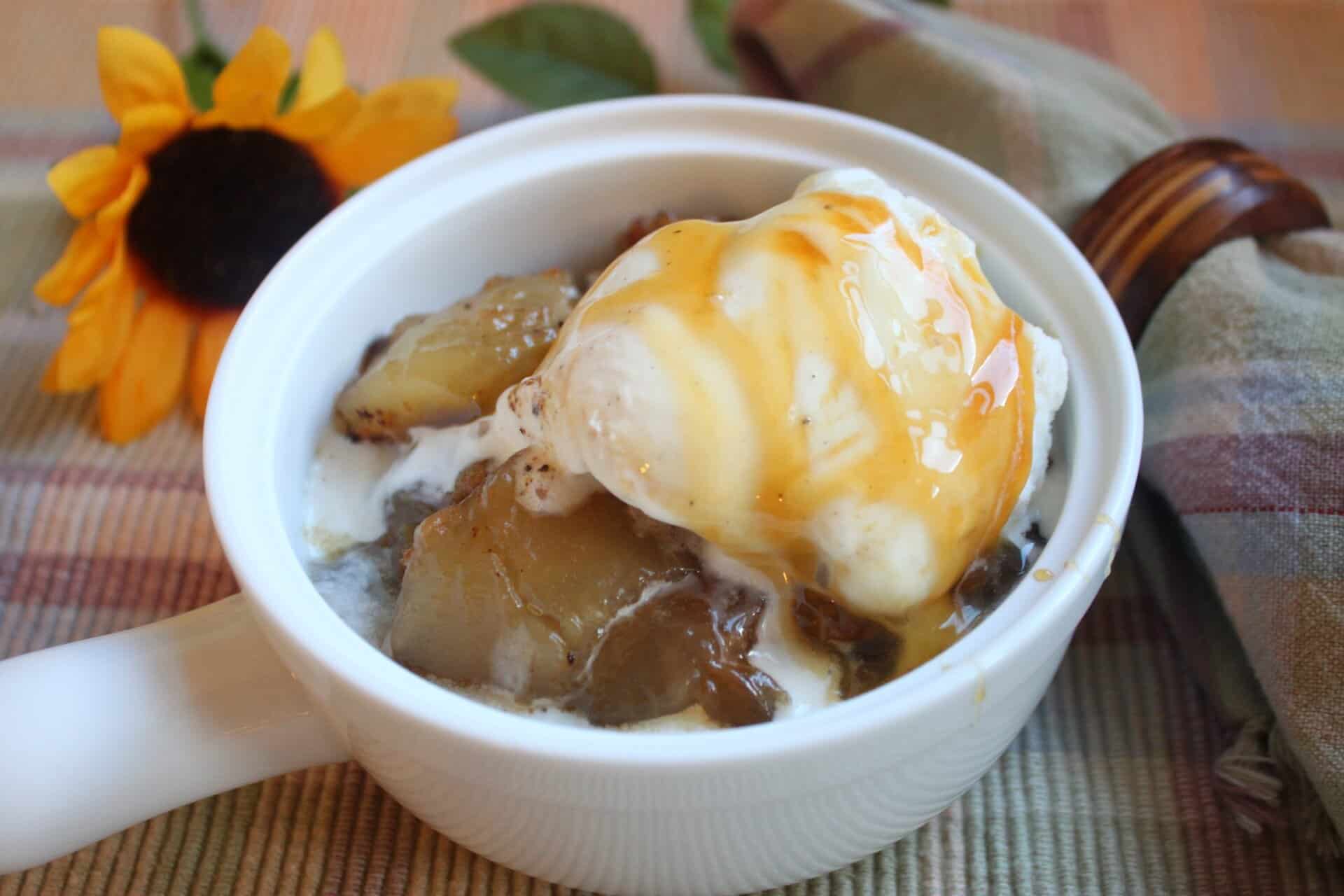 Close-up of 3 Step Crockpot Apple Spice Cake served warm with a scoop of vanilla ice cream and a drizzle of golden caramel sauce on top.