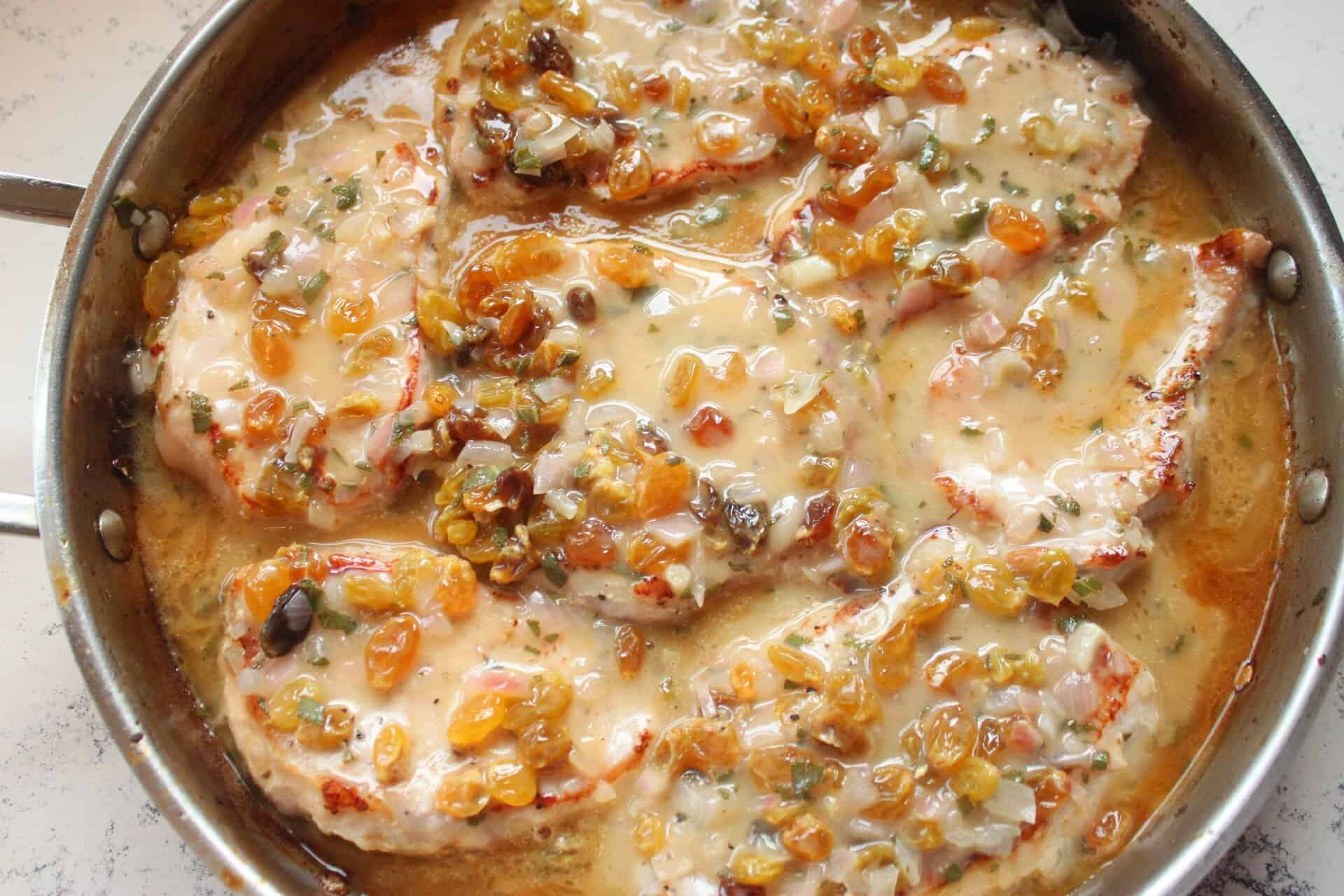 Close-up of juicy 30 Minute Apple Cider Pork Chops simmering in apple cider mustard sauce with golden raisins and fresh herbs.