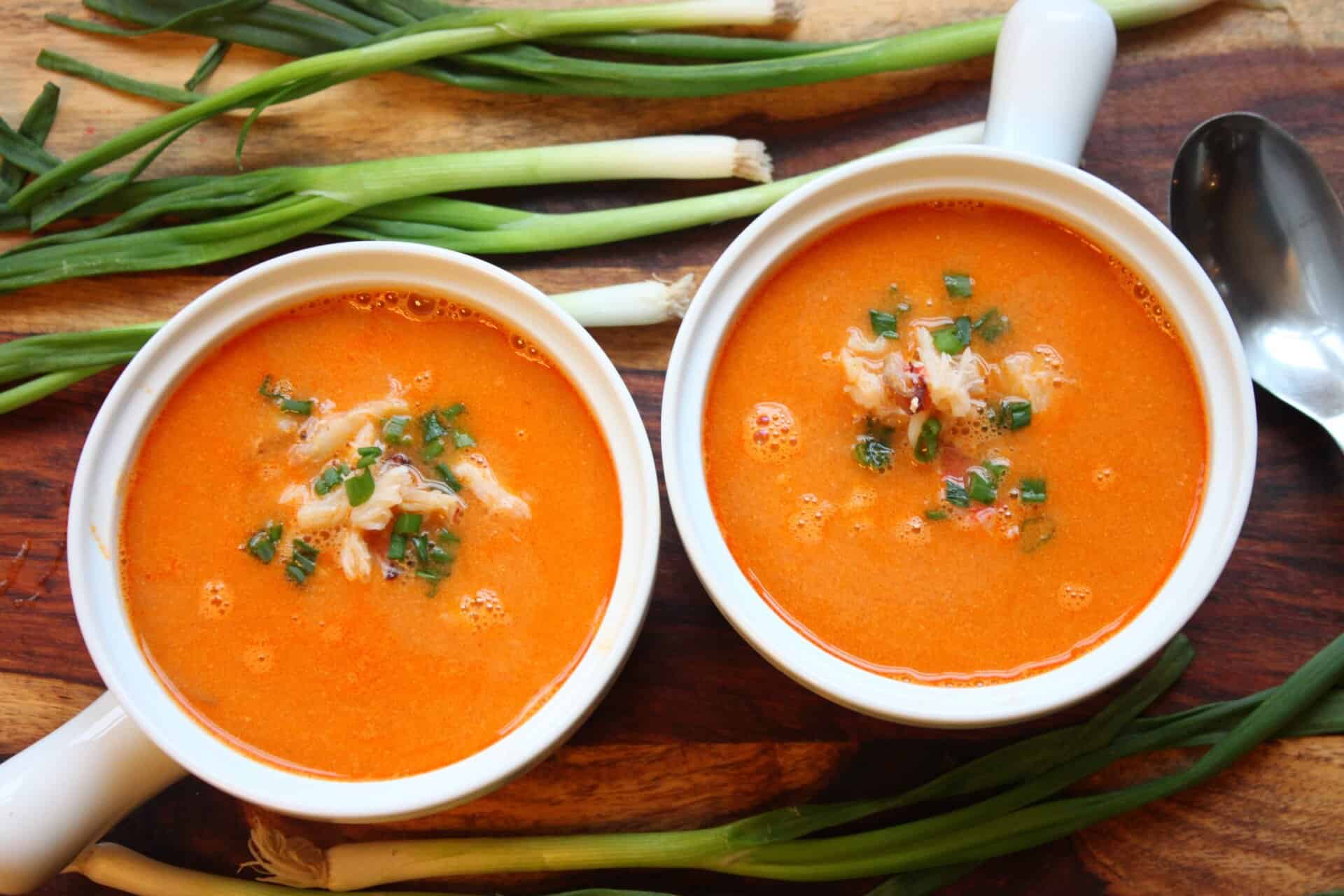 Overhead view of Dungeness crab bisque in white bowls, garnished with fresh crab meat and chopped chives, with green onions beside them.