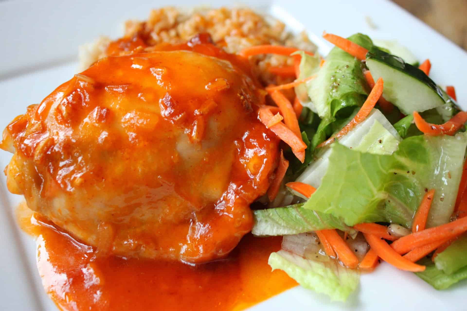 Close-up of juicy 4 Ingredient Sweet and Sour Chicken, glazed with sauce and served with rice and a fresh veggie salad.