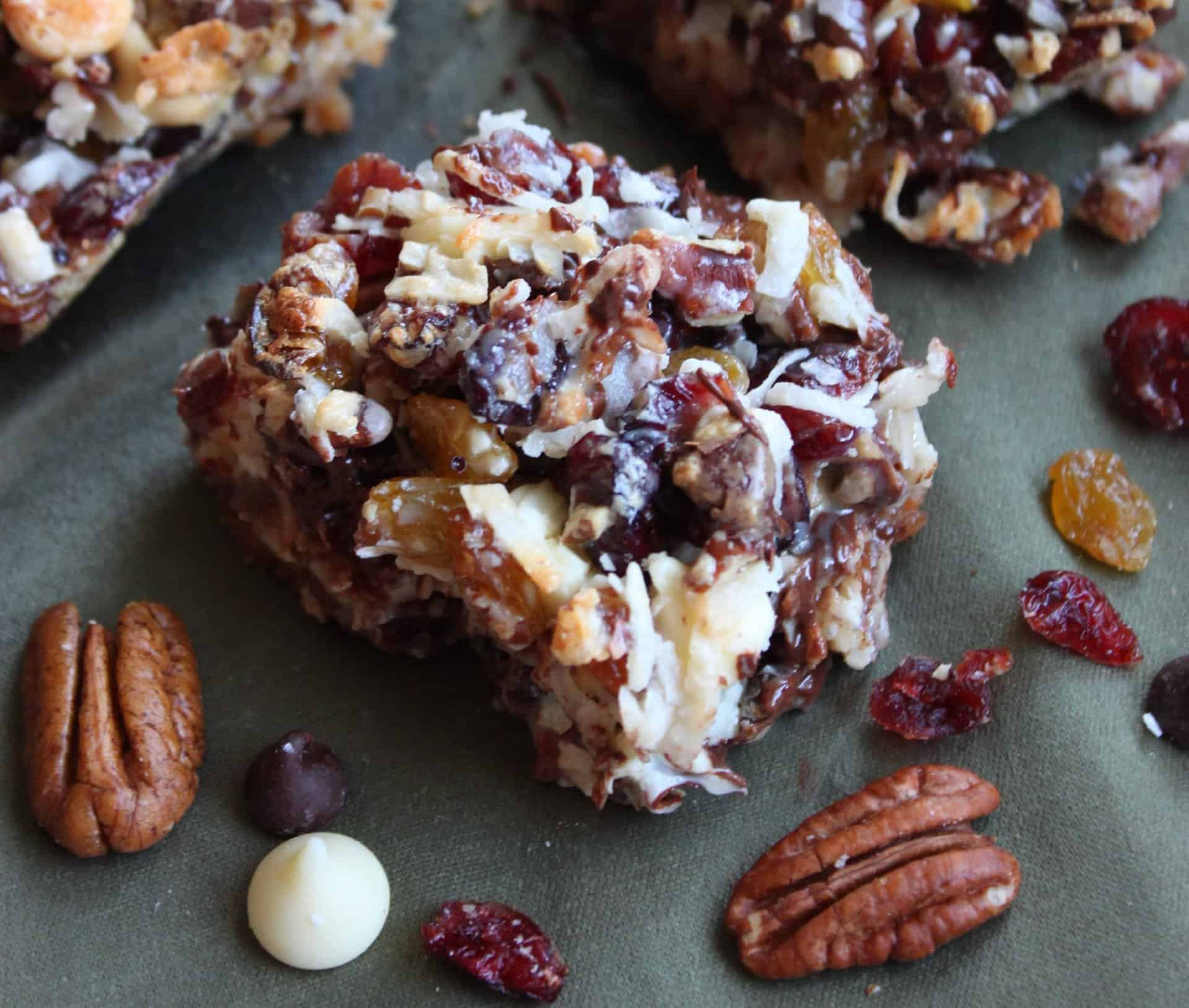 Make Coconut Pecan Bars Recipe for the Holiday Season 8 Close-up of gooey Coconut Pecan Bars filled with coconut, raisins, cranberries, and chocolate chips on a tray with pecans scattered nearby.