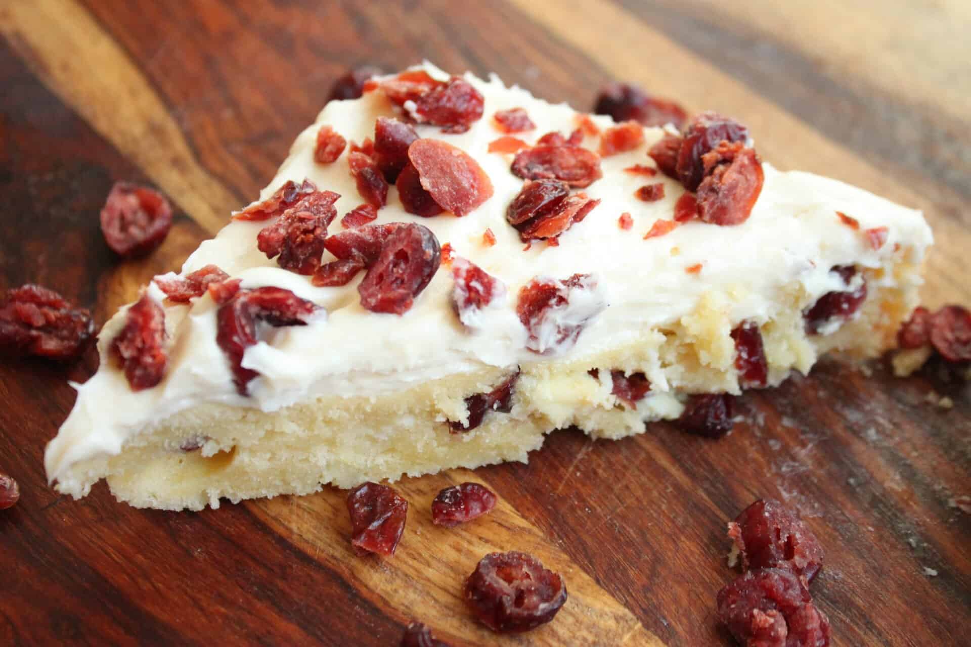 A rustic wooden board with slices of Starbucks white chocolate cranberry bliss bars, topped with cream cheese frosting and dried cranberries.