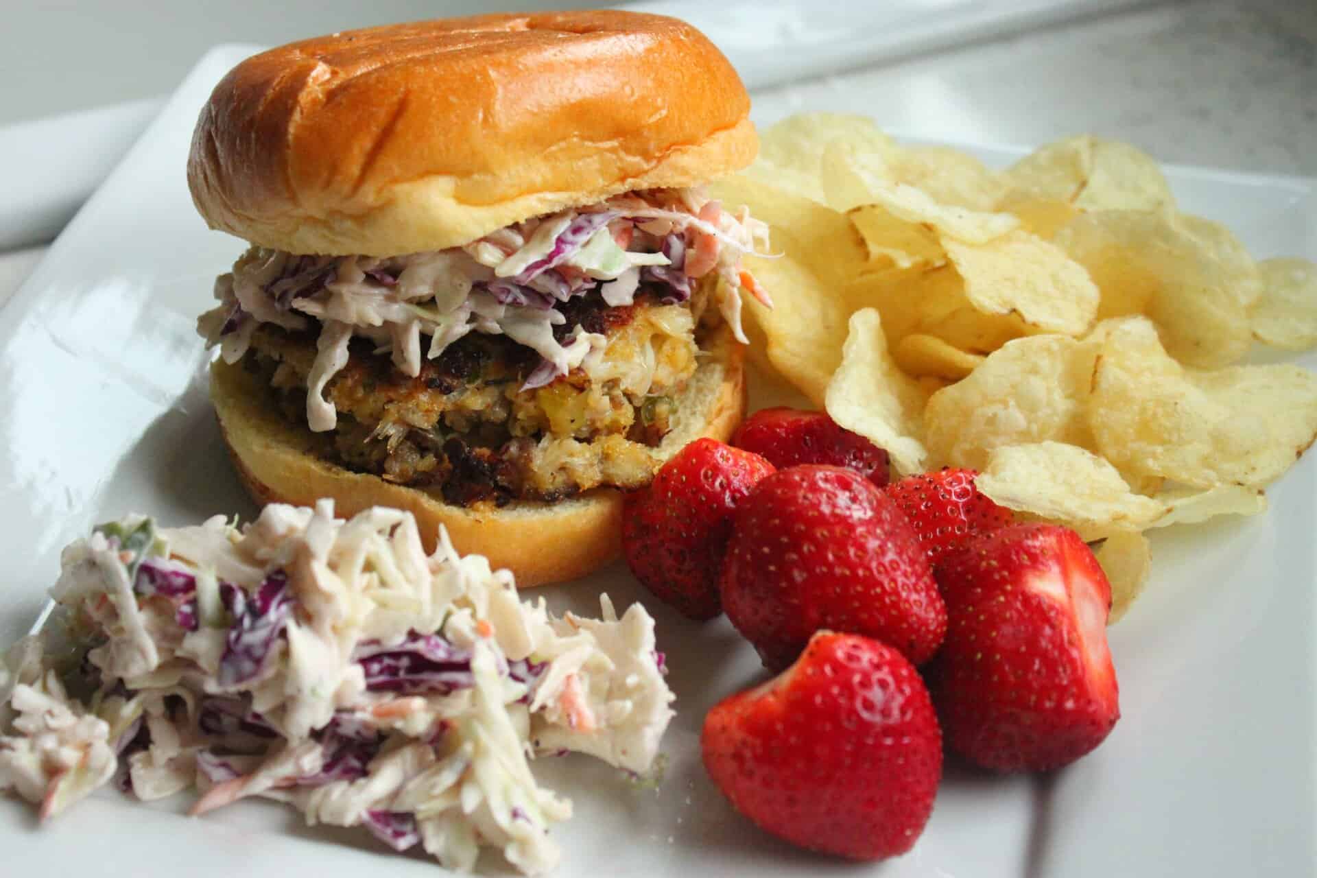 Easy Homemade Crab Cakes with Creamy Coleslaw for a Coastal Feast 14 A hero shot of Crab Cakes with Creamy Coleslaw in a brioche bun, served with potato chips and strawberries, ready to eat.