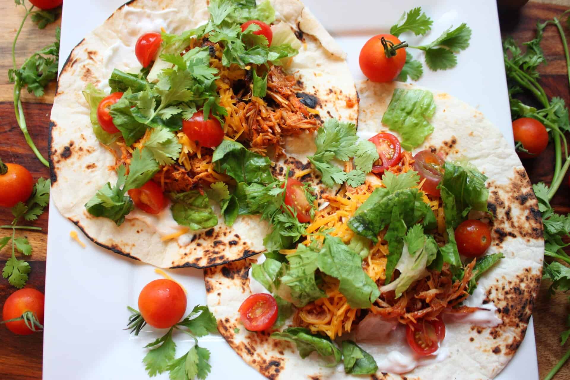 Crockpot BBQ Chicken Tacos with a Smoky Slow Cooker Blend 9 Two Crockpot BBQ Chicken Tacos loaded with shredded chicken, lettuce, cheese, cherry tomatoes, and cilantro on grilled flour tortillas.