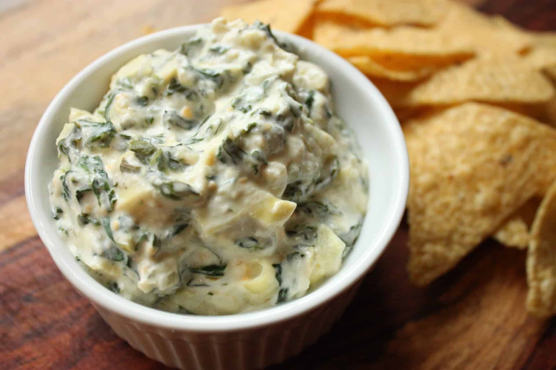 This Crockpot Spinach Artichoke Dip Will Be Your Next Party Hit 6 Crockpot Spinach Artichoke Dip served in a white bowl with golden tortilla chips in the background, perfect for parties.