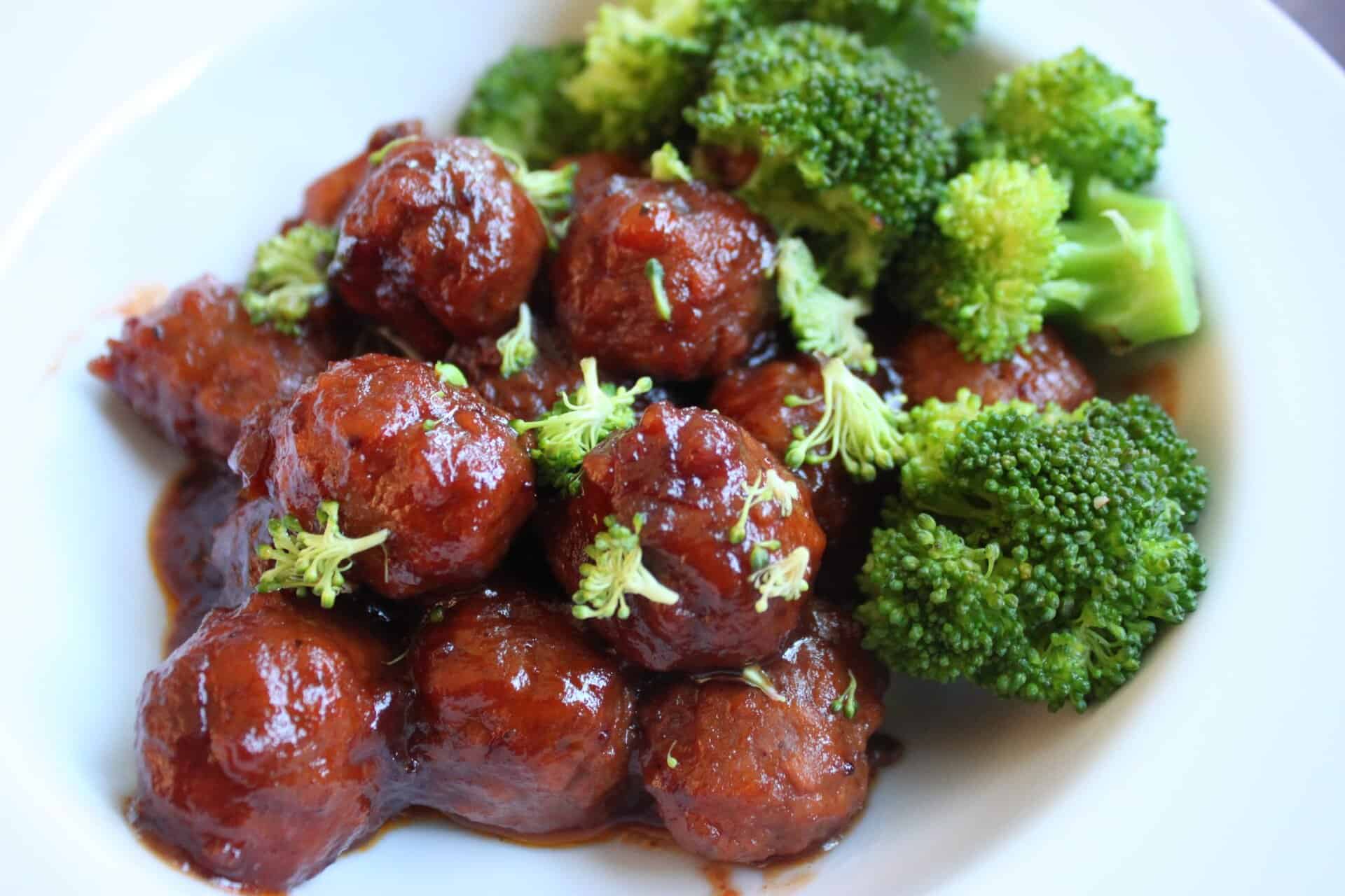 Crockpot turkey meatballs in cranberry sauce served on a white plate with broccoli florets for a balanced, colorful meal.