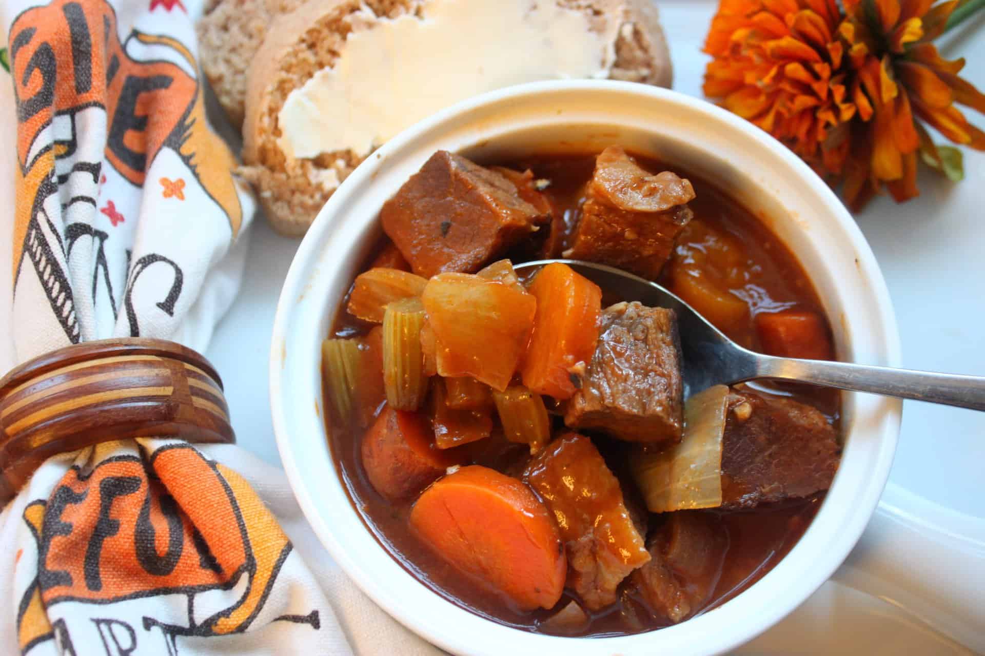 Spoonful of Crockpot vegetable beef burgundy lifted from a bowl with carrots, onions, and beef, paired with bread on the side.