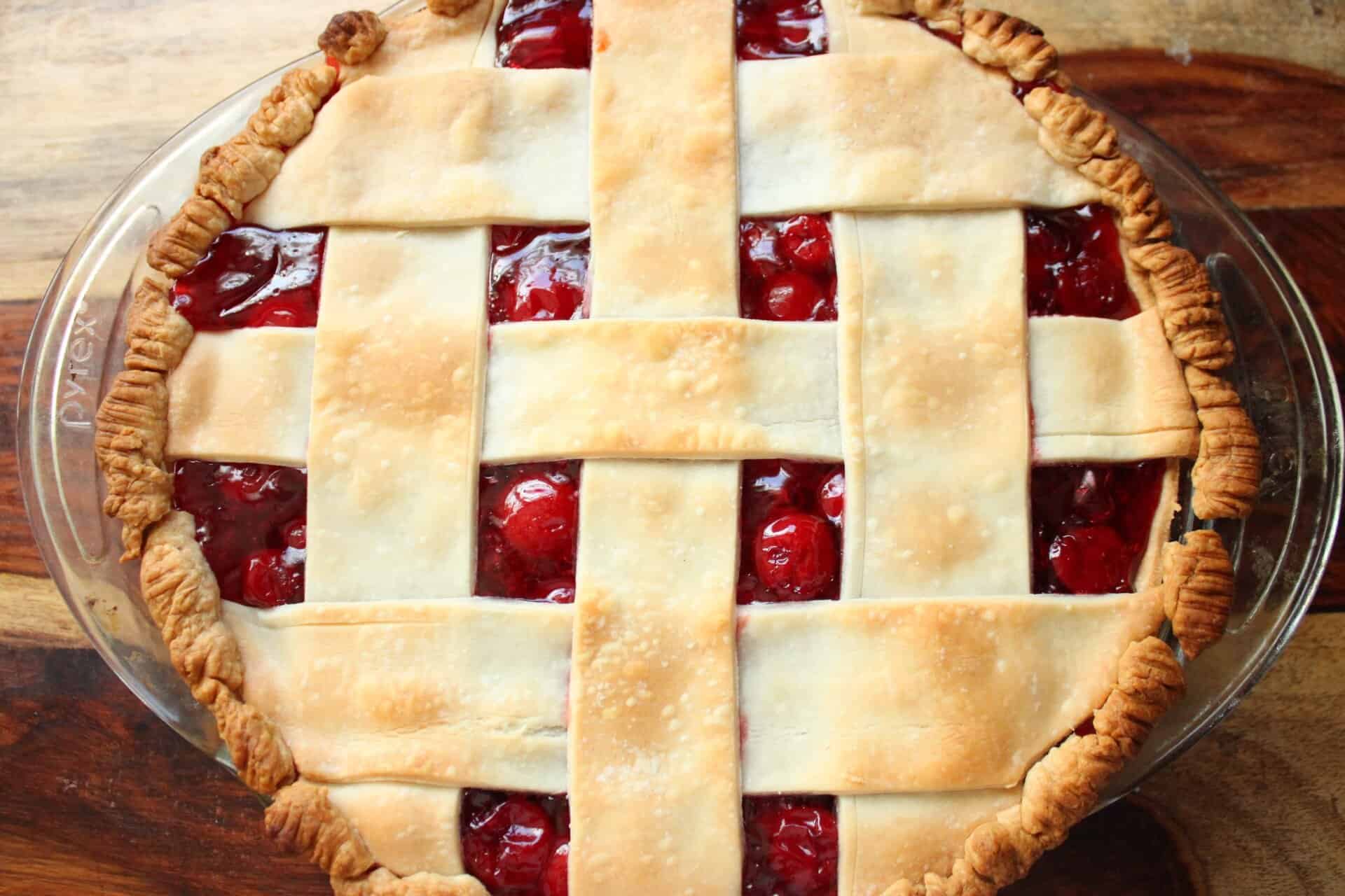 A latticed cherry pie baked to golden perfection, with a crisp crust and bright red cherry filling peeking through the lattice.