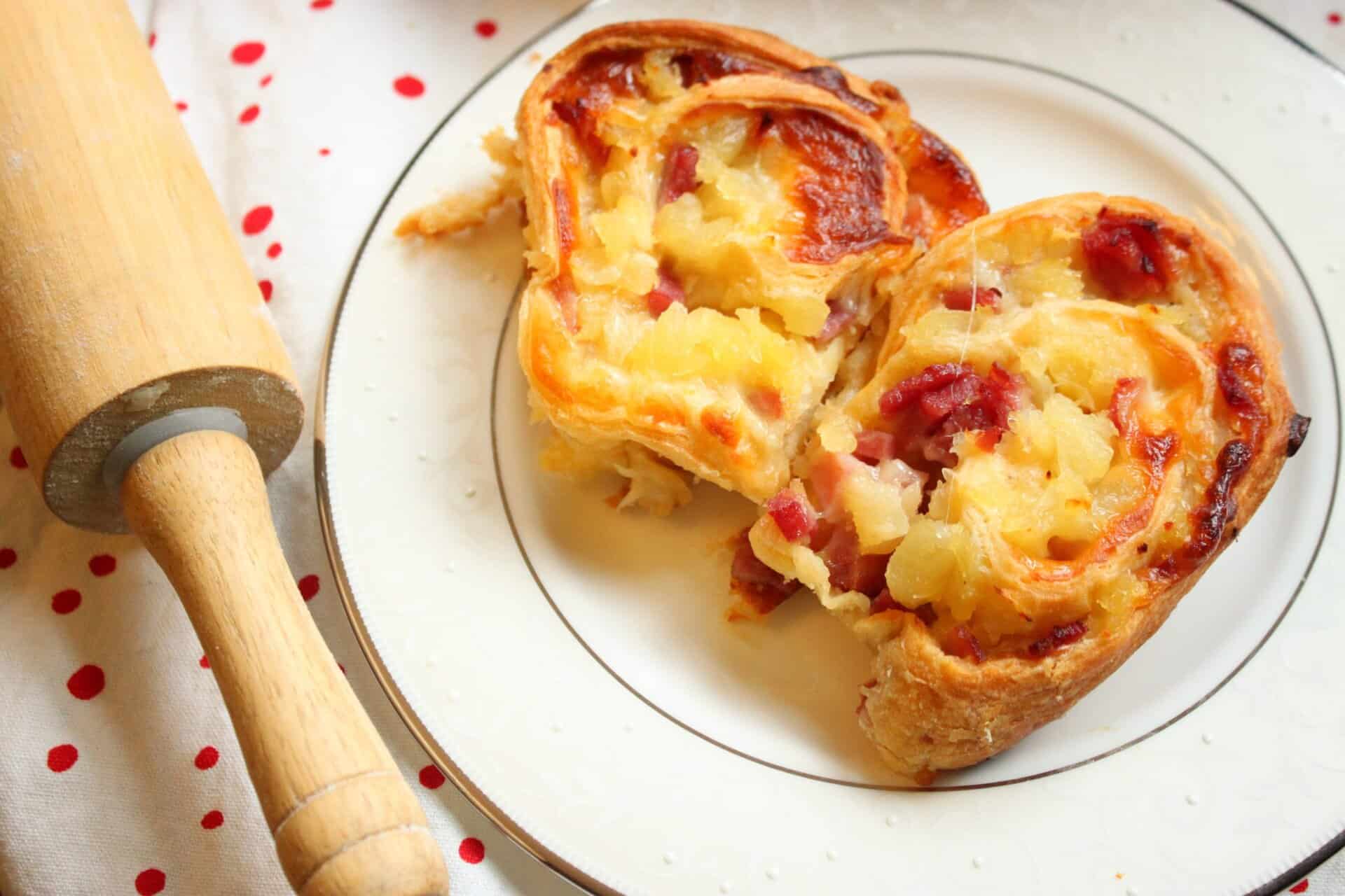 A close-up shot of two golden-brown ham and pineapple pinwheels on a plate, showing the layers of ham, cheese, and pineapple.