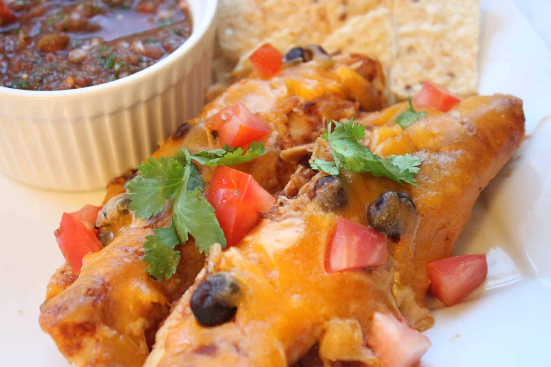 Freshly baked healthy chicken enchiladas on a plate, topped with tomatoes, cilantro, and melted cheese.
