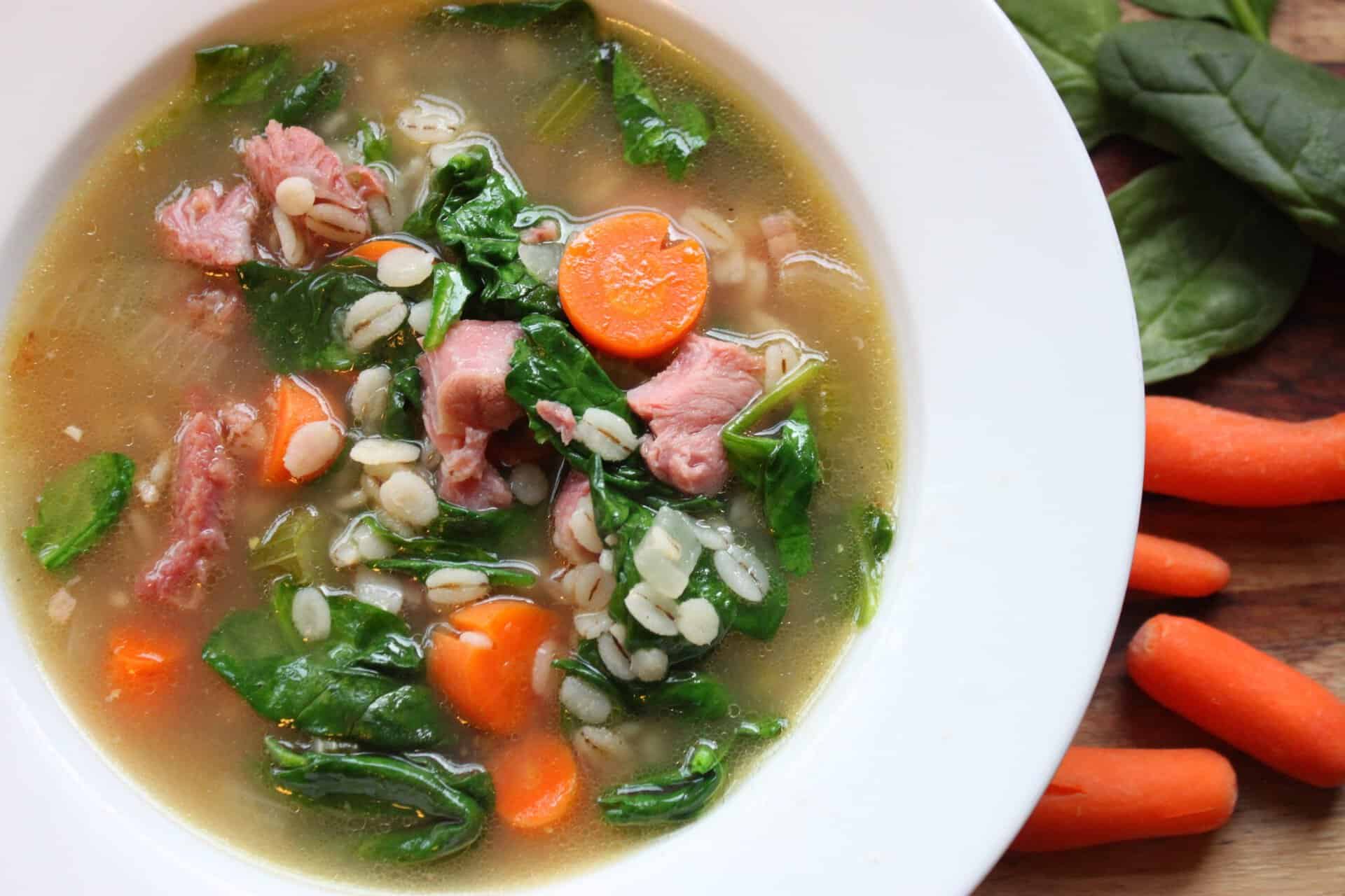 A close-up bowl of healthy ham and barley soup with spinach, carrots, and tender ham pieces, making a comforting and flavorful meal.
