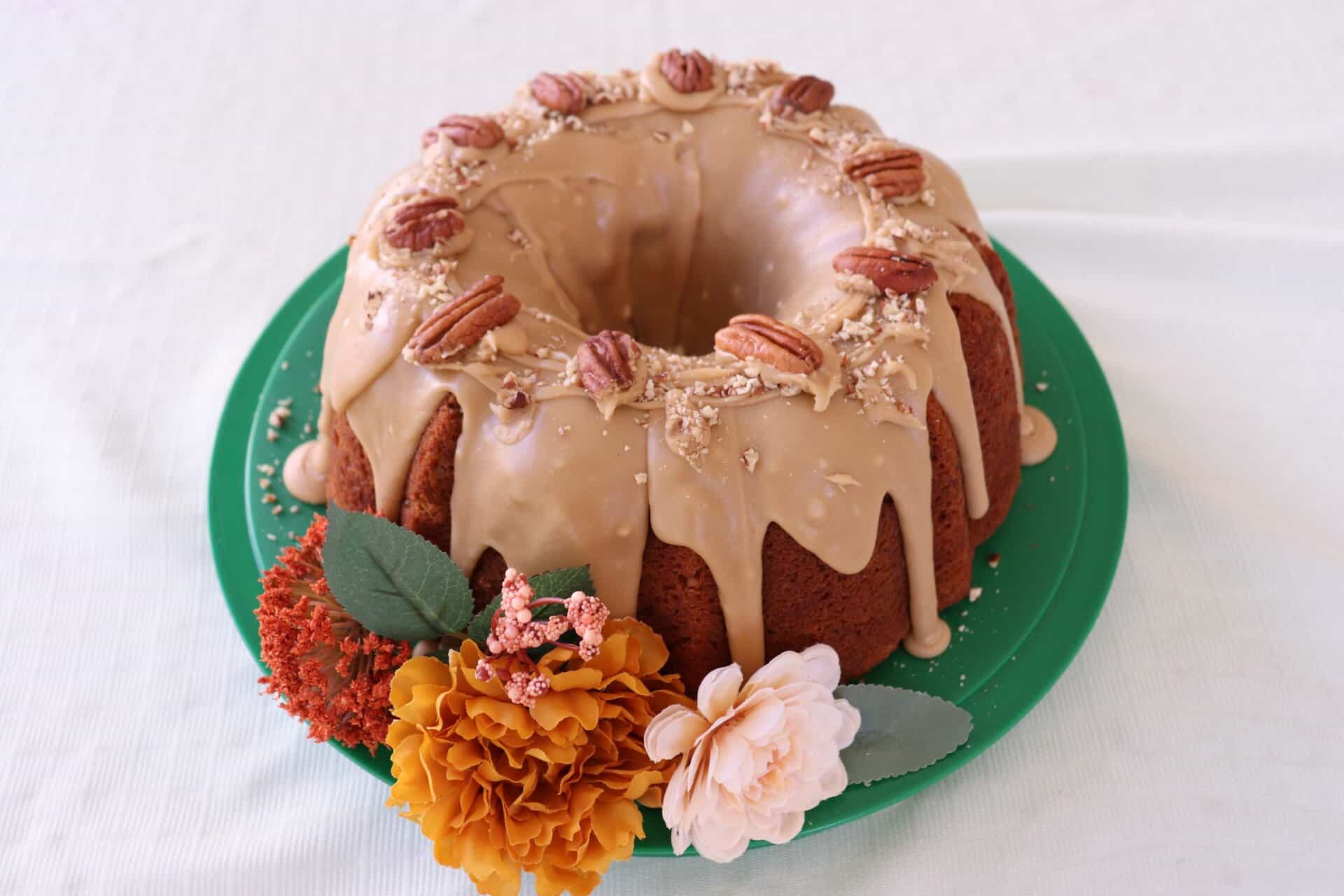 Perfect for Fall Parties: Pumpkin Pecan Bundt Cake with Brown Sugar Icing 13 Pumpkin pecan bundt cake with brown sugar icing drizzled down the sides, topped with whole pecans and surrounded by autumn flowers.