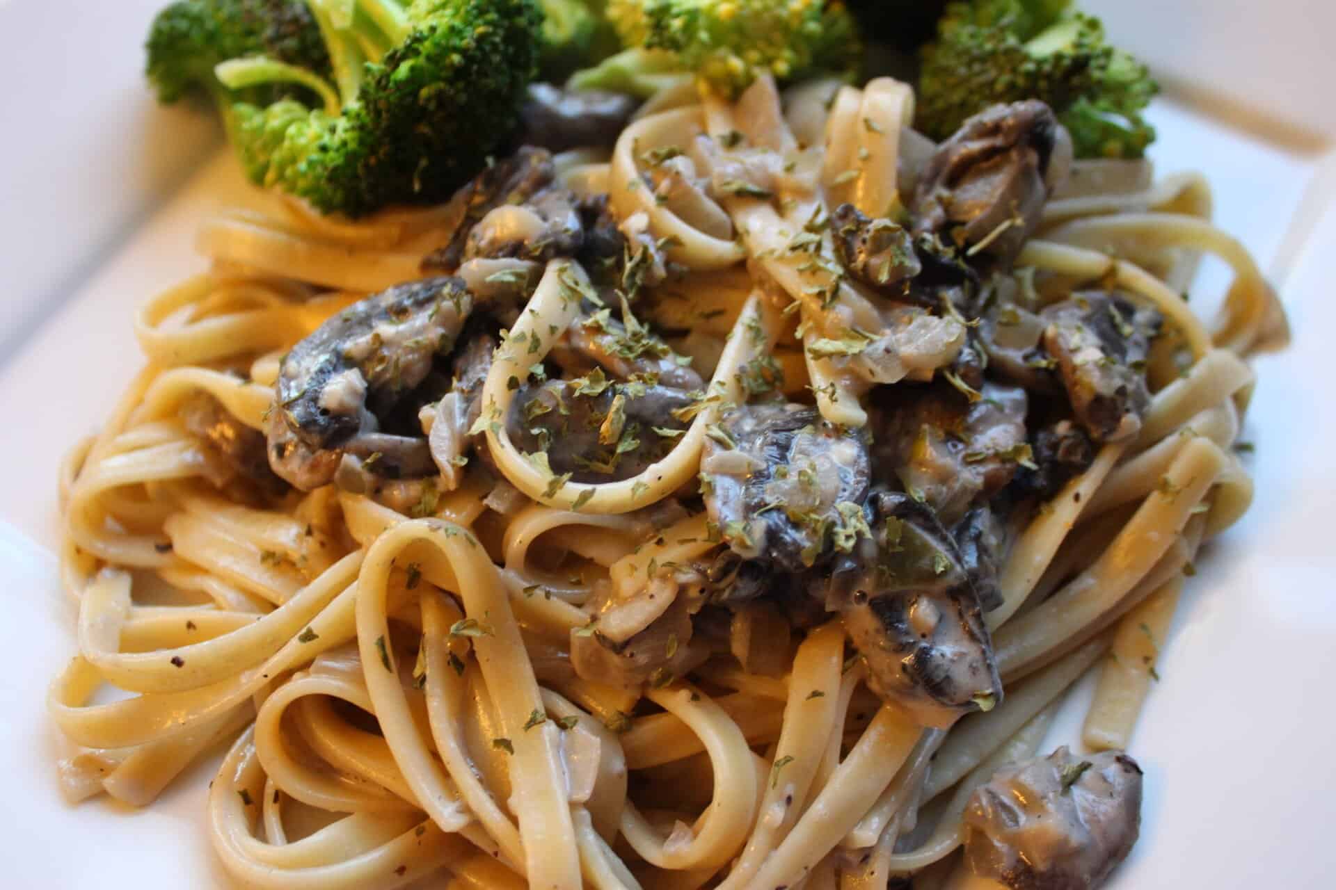 A bowl of skinny creamy fettuccine Alfredo topped with mushrooms and herbs, served with broccoli for a healthy pasta meal.