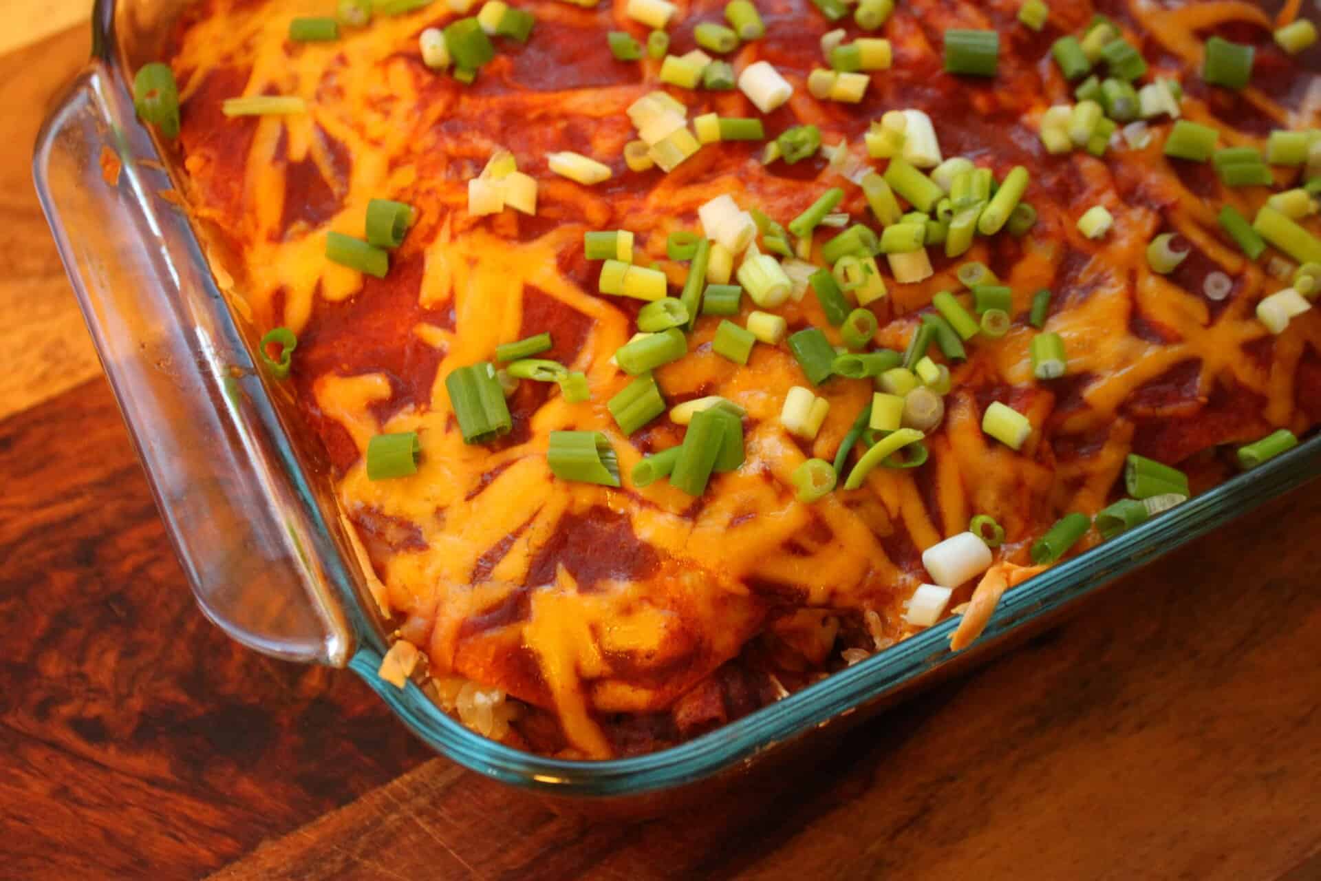 A baking dish of spicy chicken enchiladas topped with melted cheese, green onions, and a rich red sauce, fresh from the oven.